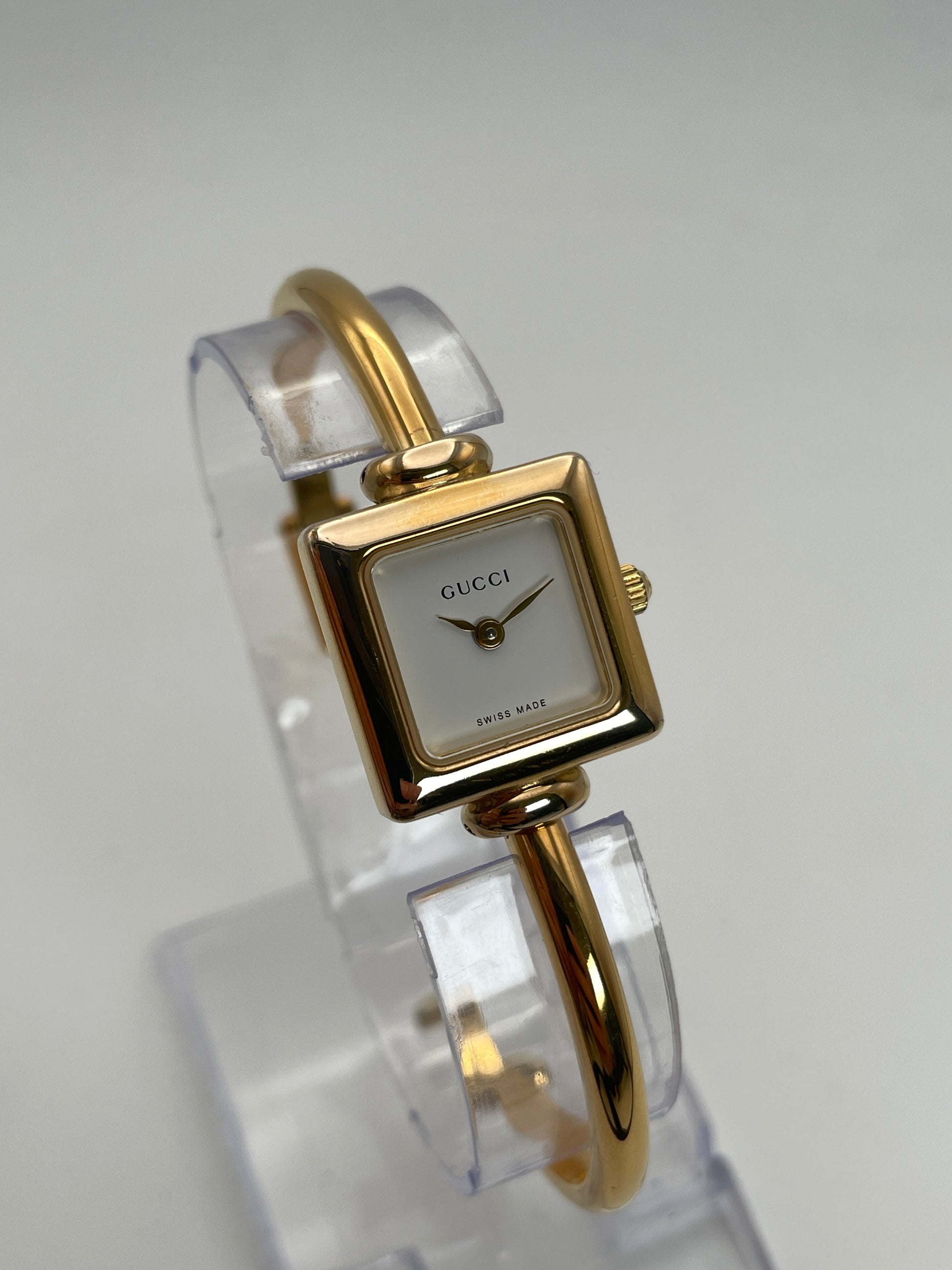 Front view of Gucci 1900L gold watch with a square case and white dial, featuring a gold bangle bracelet.