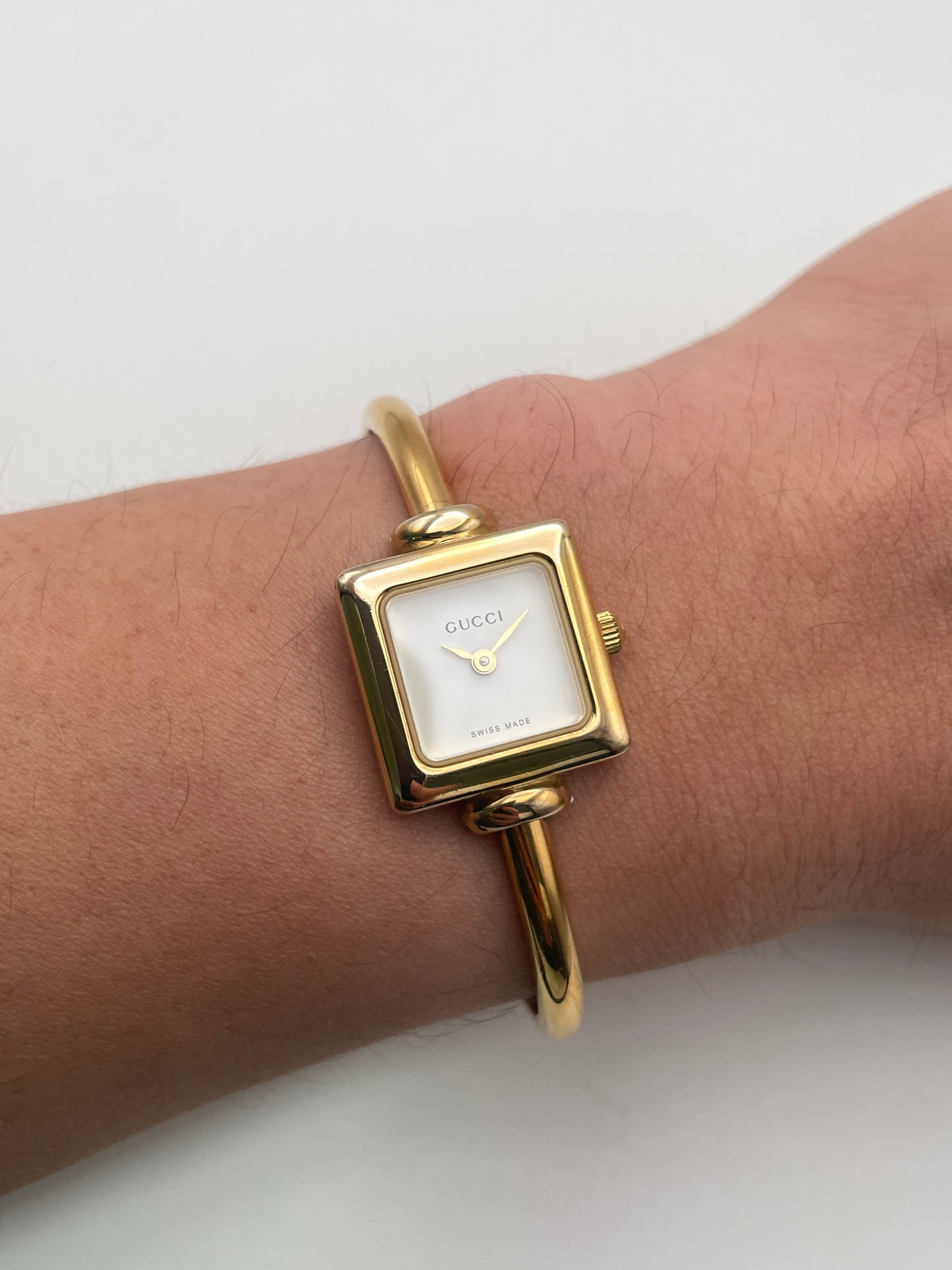 Wrist shot of Gucci 1900L gold watch with a square case and white dial, featuring a gold bangle bracelet.