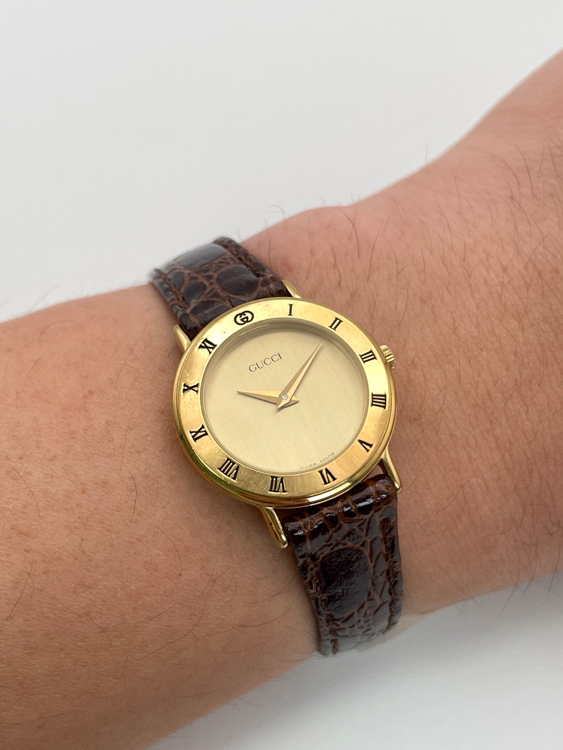 Wrist shot of the Gucci 3000.2.L vintage ladies' watch in gold with a brown leather strap.

