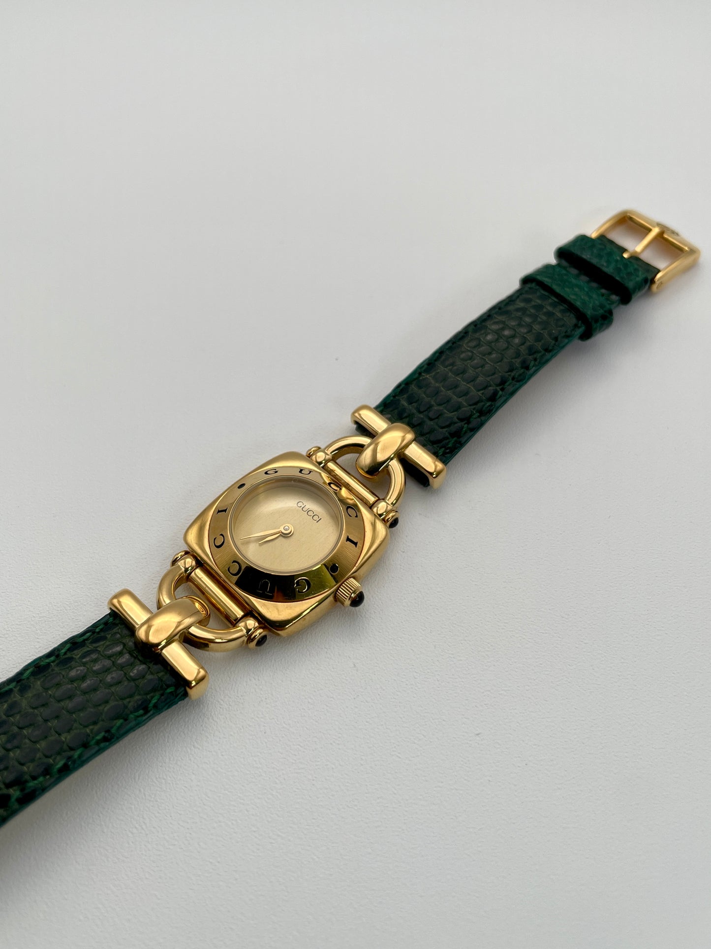 Diagonal view of a Gucci 6300L ladies' watch, highlighting the  gold square case, gold dial, and green lizard skin strap.