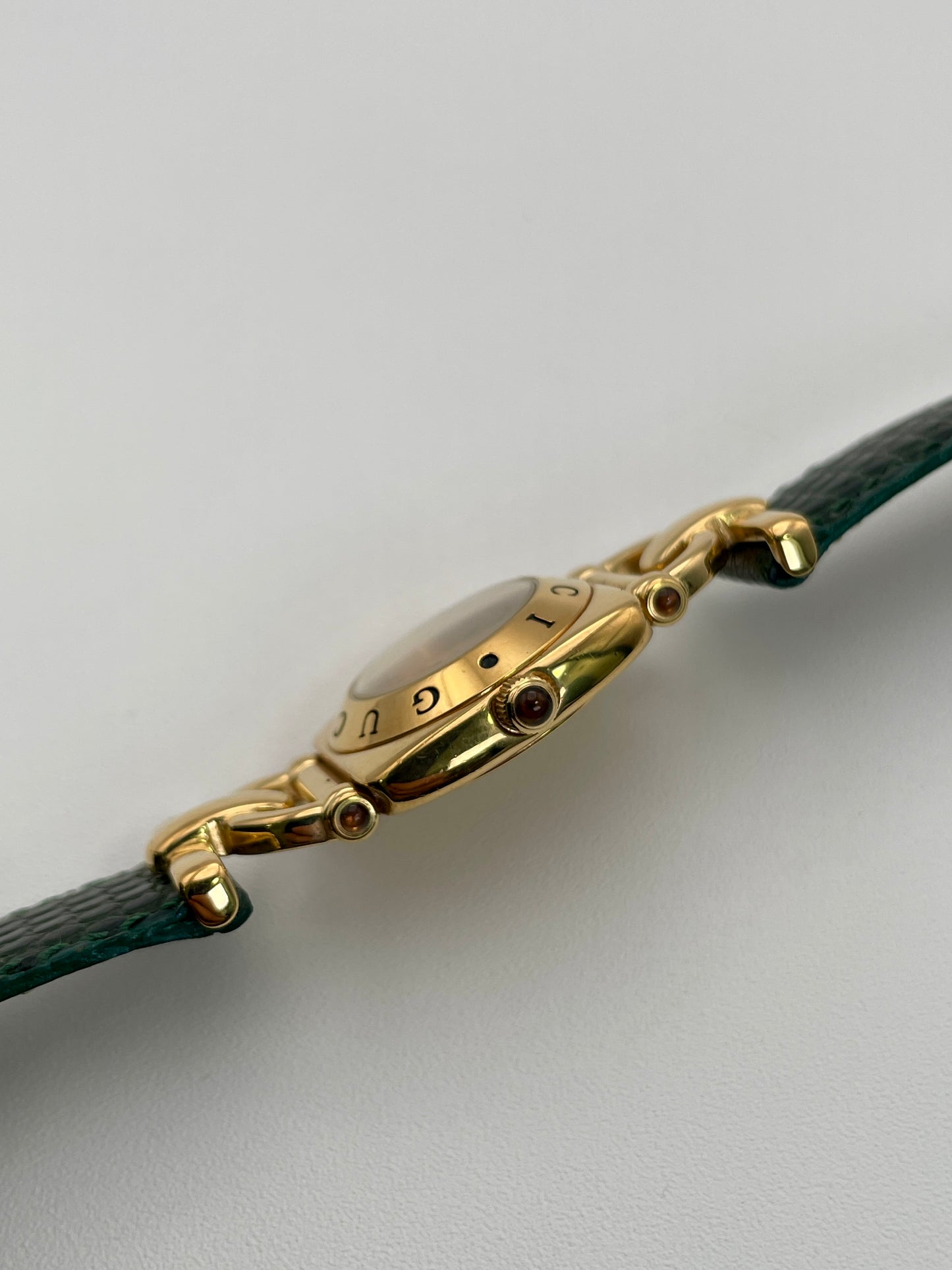 Side view of a Gucci 6300L ladies' watch, showcasing the  gold case and crown with a green accent, paigreen with a green lizard skin strap.
