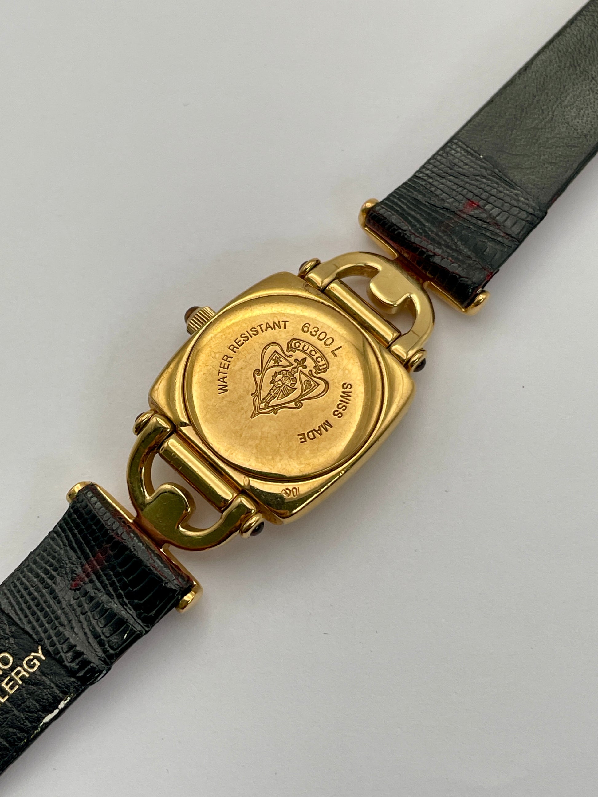 Caseback view of a Gucci 6300L ladies' watch with an engraved gold-tone back, detailing the model number and water resistance.