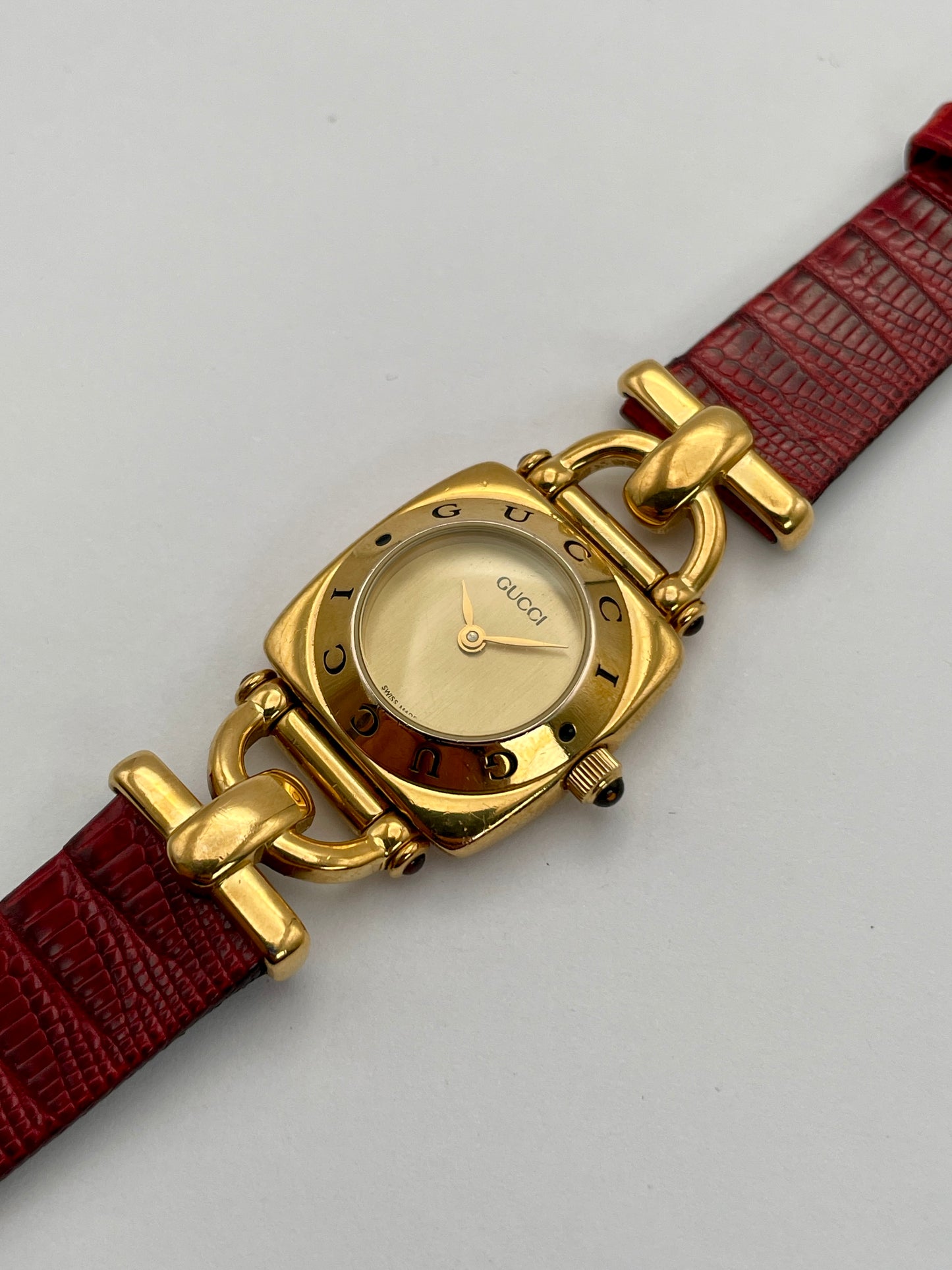 Diagonal view of a Gucci 6300L ladies' watch, highlighting the gold-tone square case, gold dial, and red leather strap.