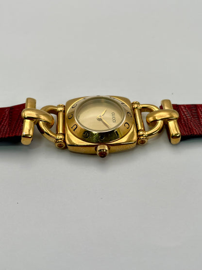 Side view of a Gucci 6300L ladies' watch, showcasing the gold-tone case and crown with a red accent, paired with a red leather strap.