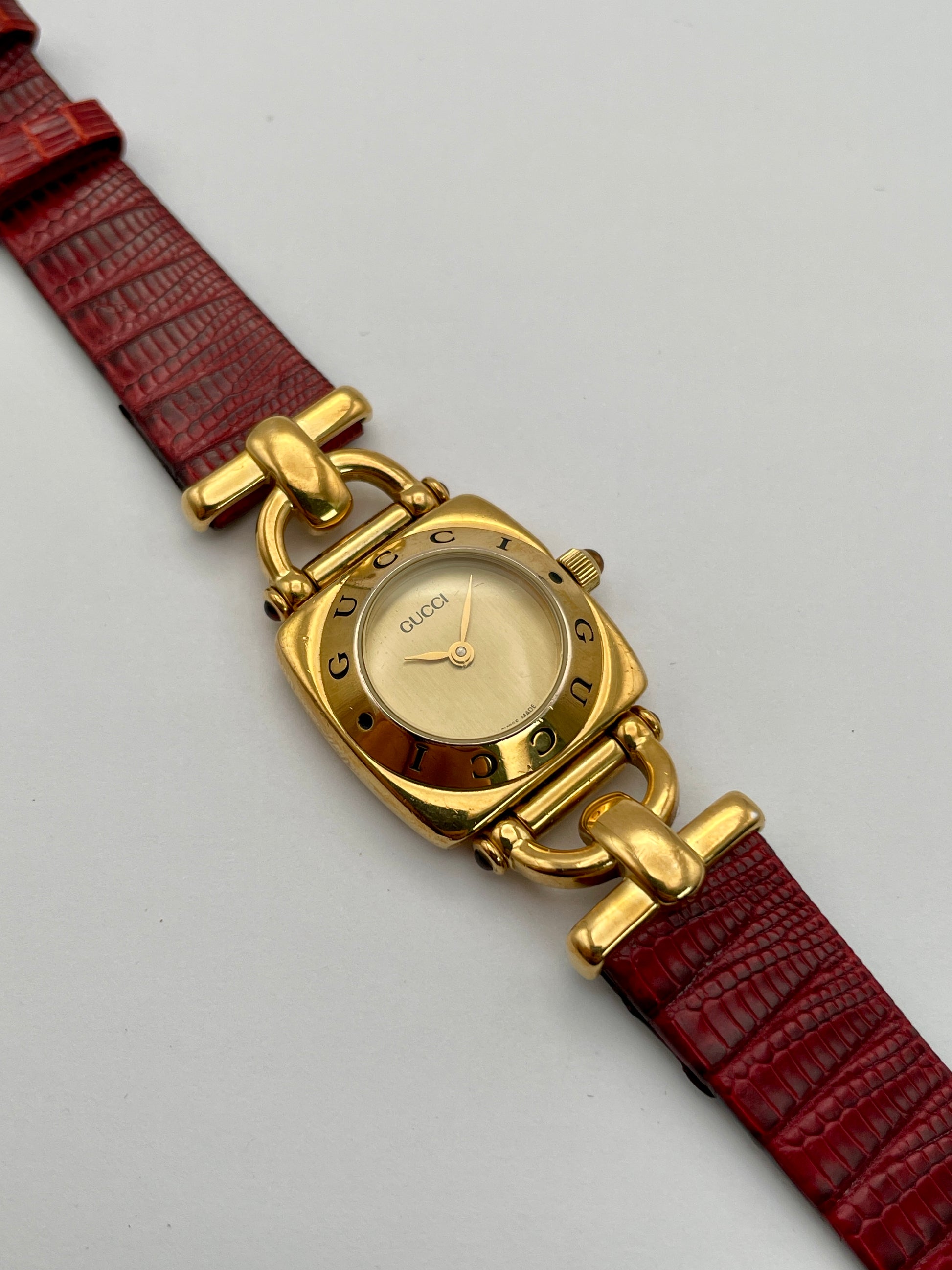 Top view of a Gucci 6300L ladies' watch with a gold-tone square case, gold dial, and red leather strap, showing the intricate design and logo.