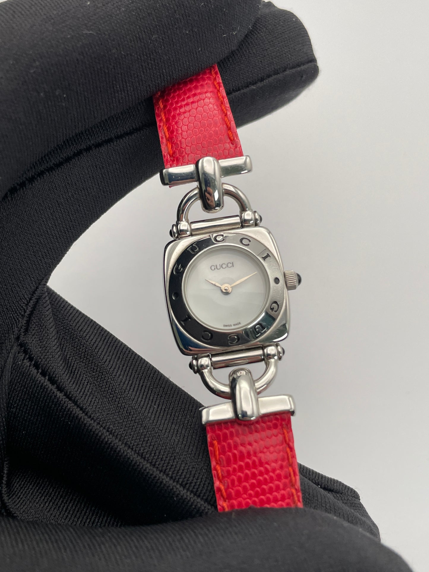 Close-up view of a Gucci 6300L ladies' watch, focusing on the stainless steel square case, white dial, and red lizard skin strap.
