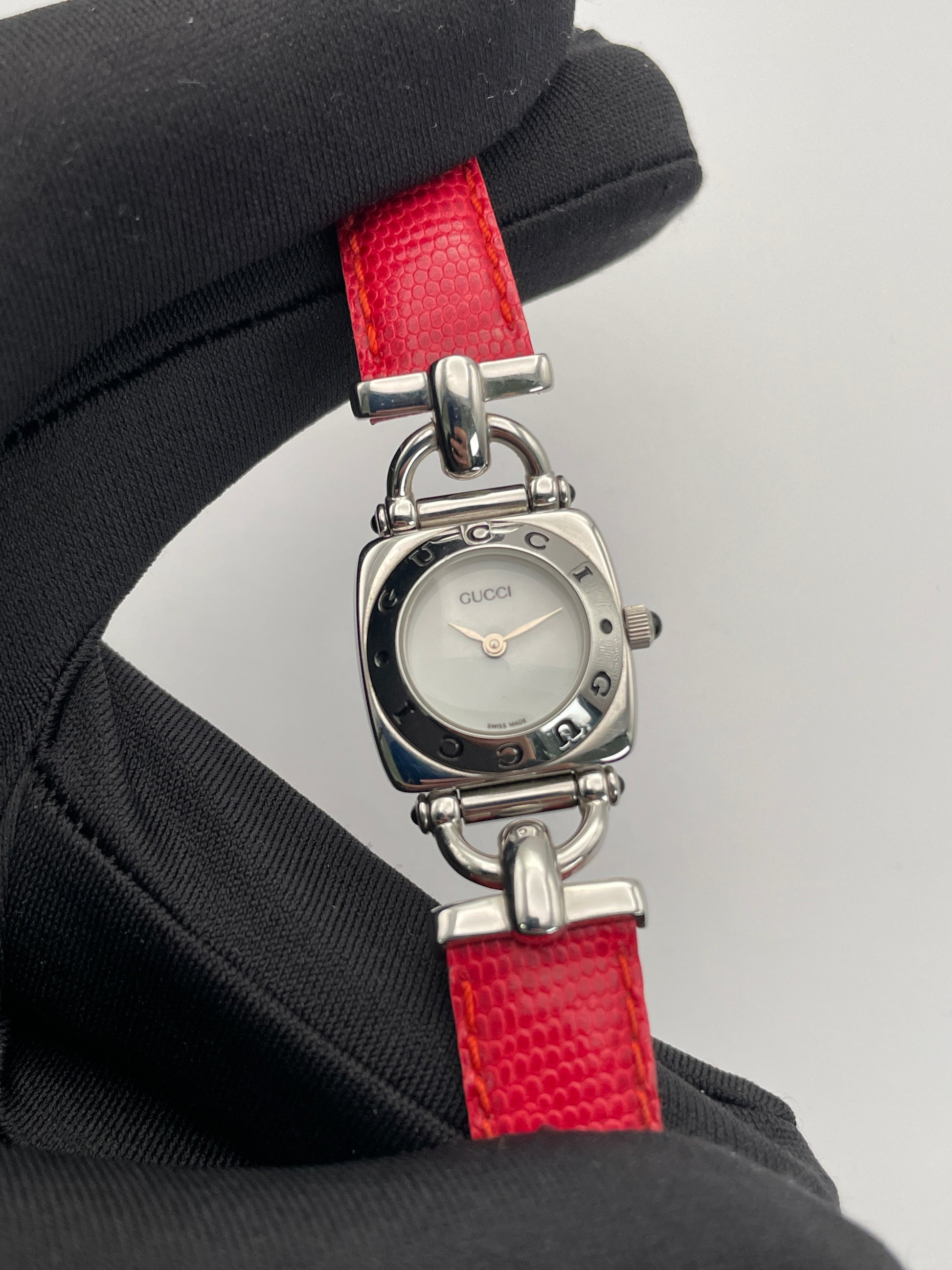 Close-up view of a Gucci 6300L ladies' watch, focusing on the stainless steel square case, white dial, and red lizard skin strap.