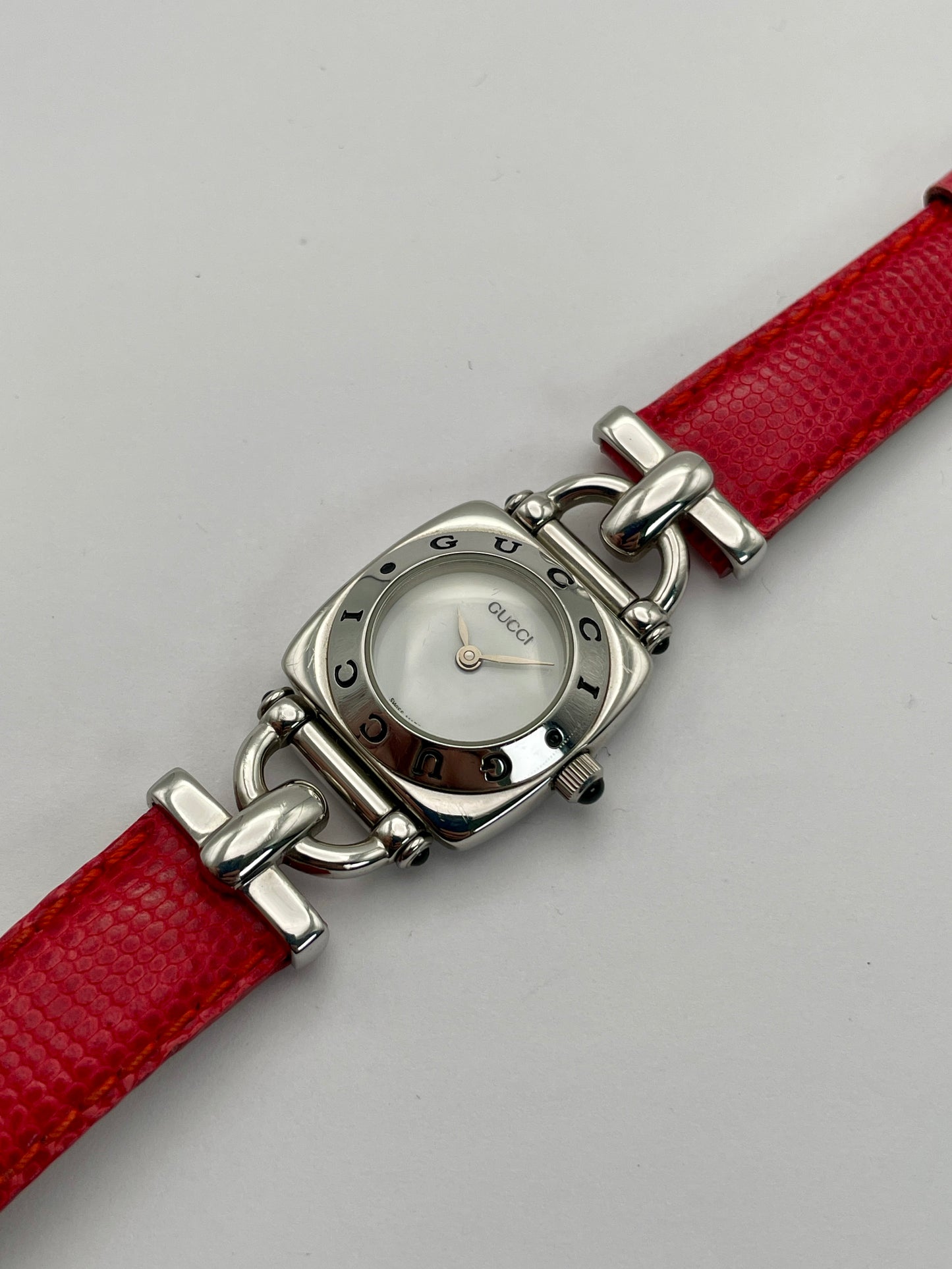 Diagonal view of a Gucci 6300L ladies' watch, highlighting the stainless steel square case, white dial, and red lizard skin strap.
