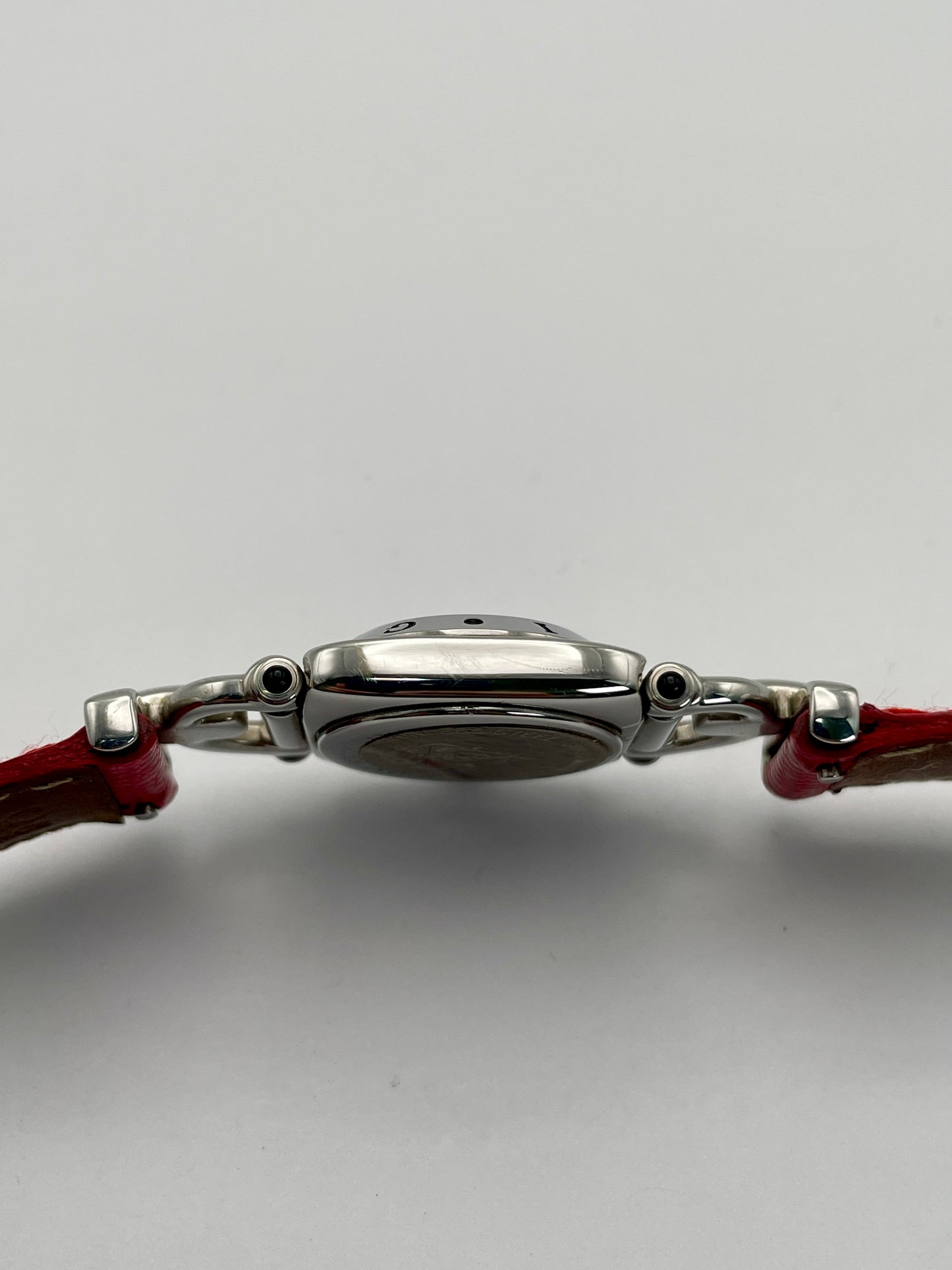 Side profile of a Gucci 6300L ladies' watch, emphasizing the stainless steel case and the connection to the red lizard skin strap.
