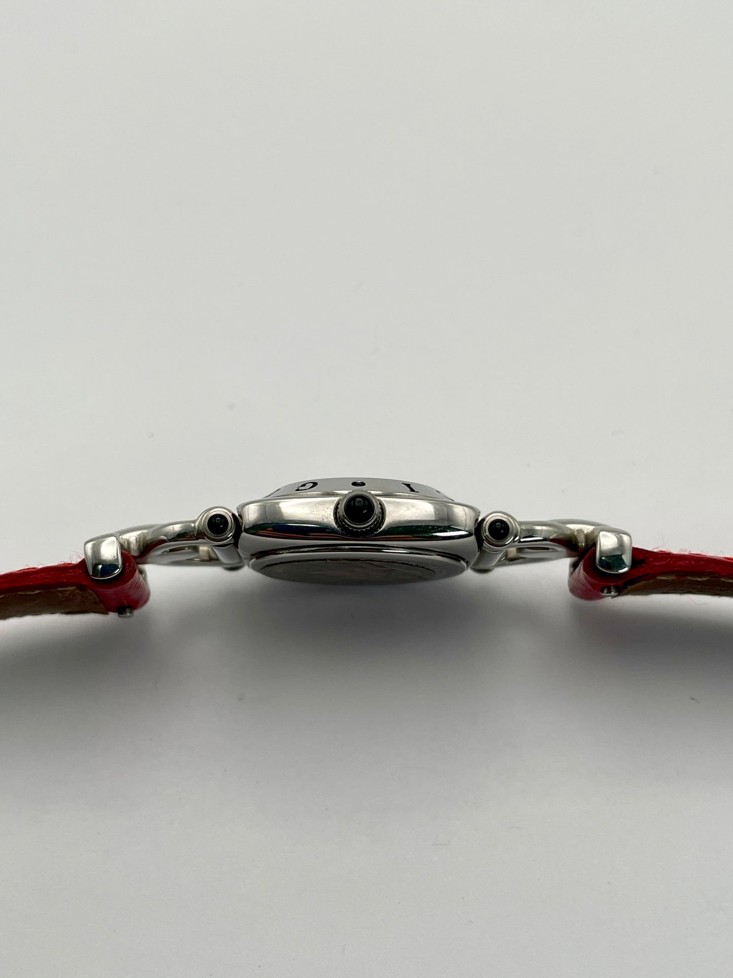 Side view of a Gucci 6300L ladies' watch, showcasing the stainless steel case and crown with a red accent, paired with a red lizard skin strap.