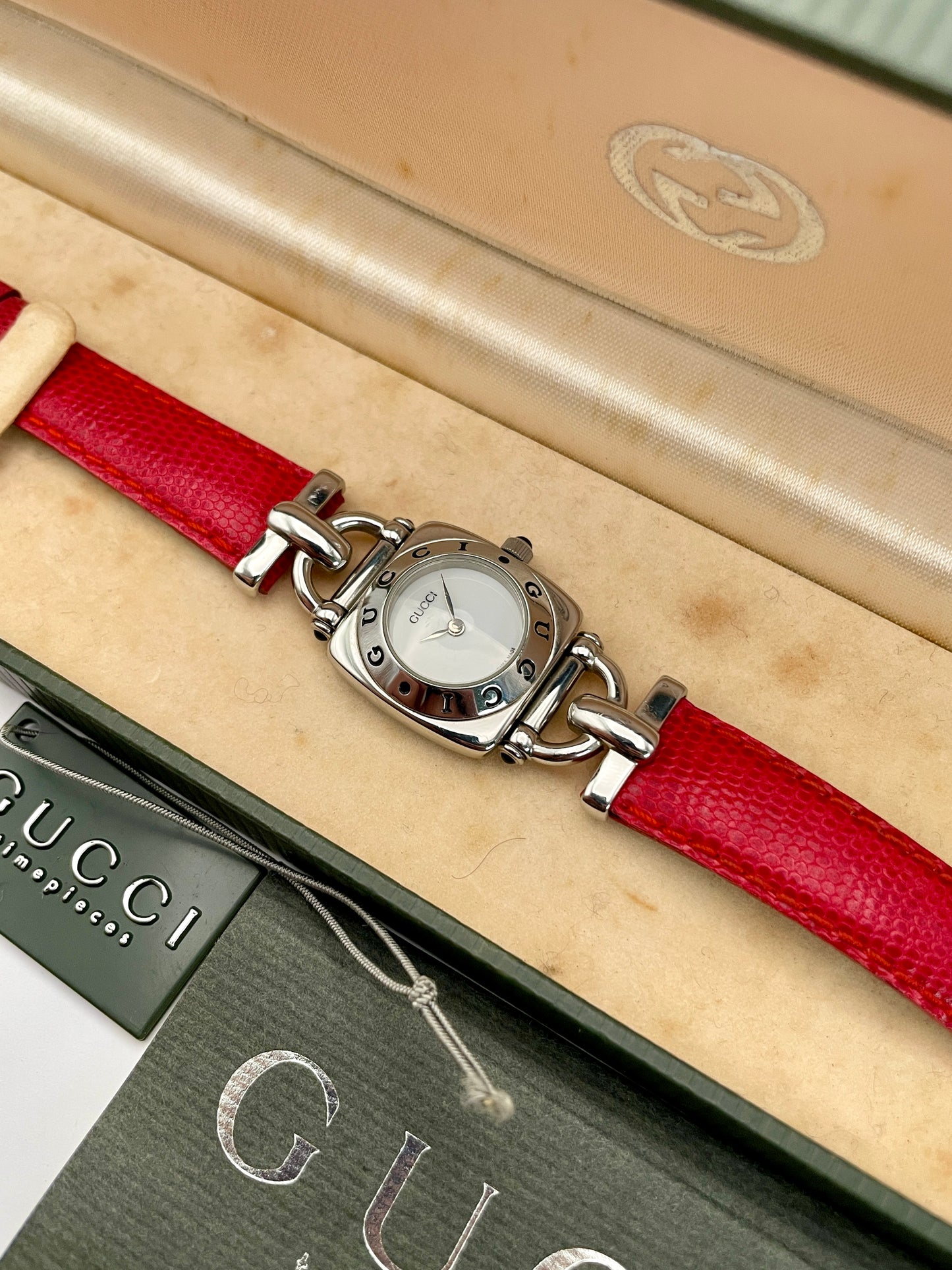 Top view of a Gucci 6300L ladies' watch featuring a stainless steel square case with rounded edges, white dial, and red lizard skin strap, in its original box and papers.