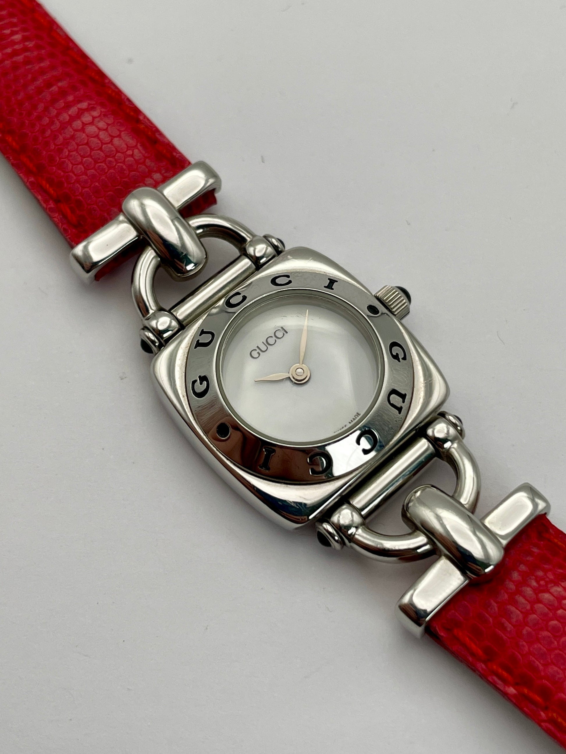 Top view of a Gucci 6300L ladies' watch with a stainless steel square case, white dial, and red lizard skin strap, showing the intricate design and logo.