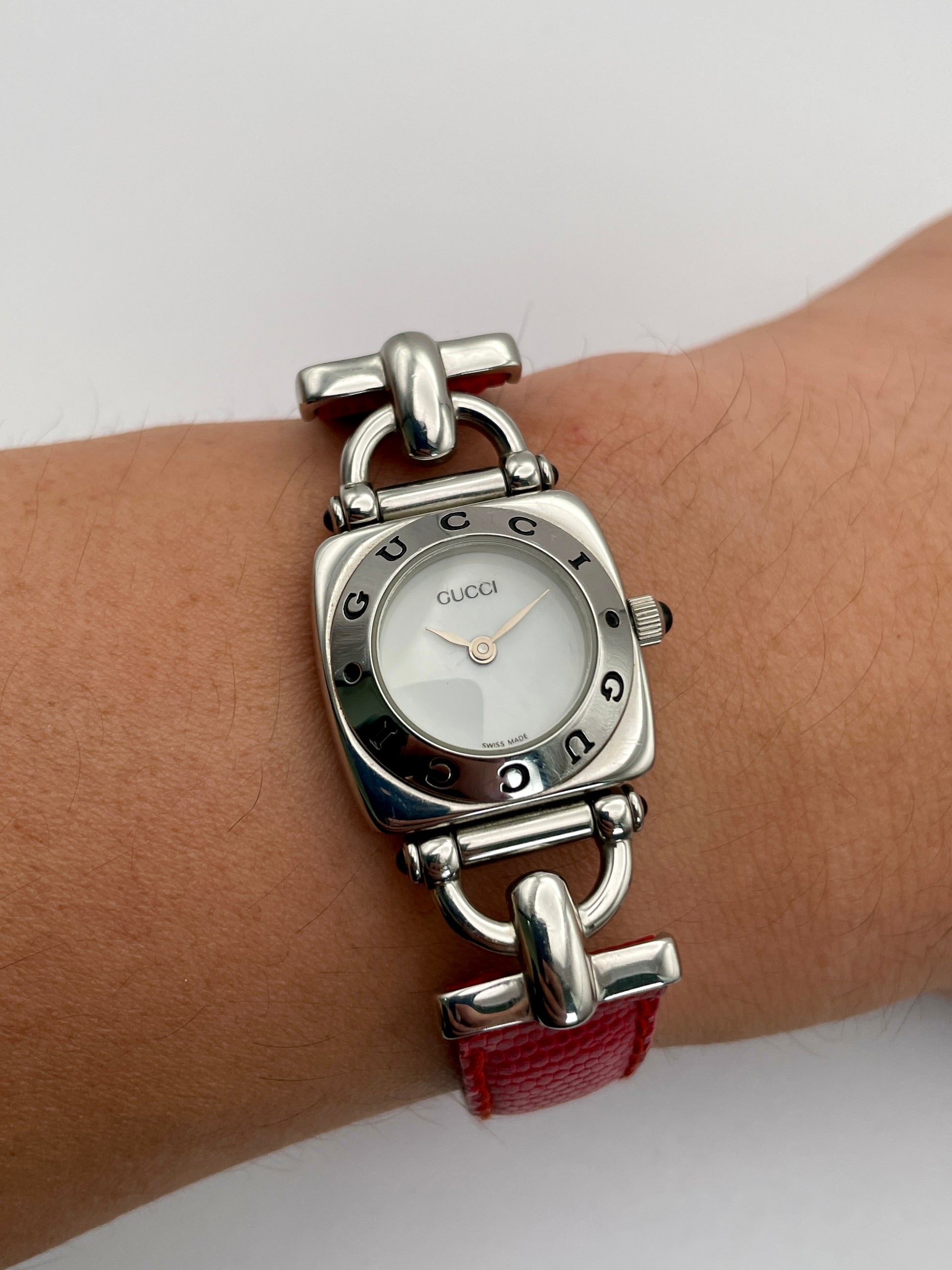 Gucci 6300L ladies' watch with a stainless steel square case, white dial, and red lizard skin strap, elegantly worn on the wrist, highlighting its refined design and fit.