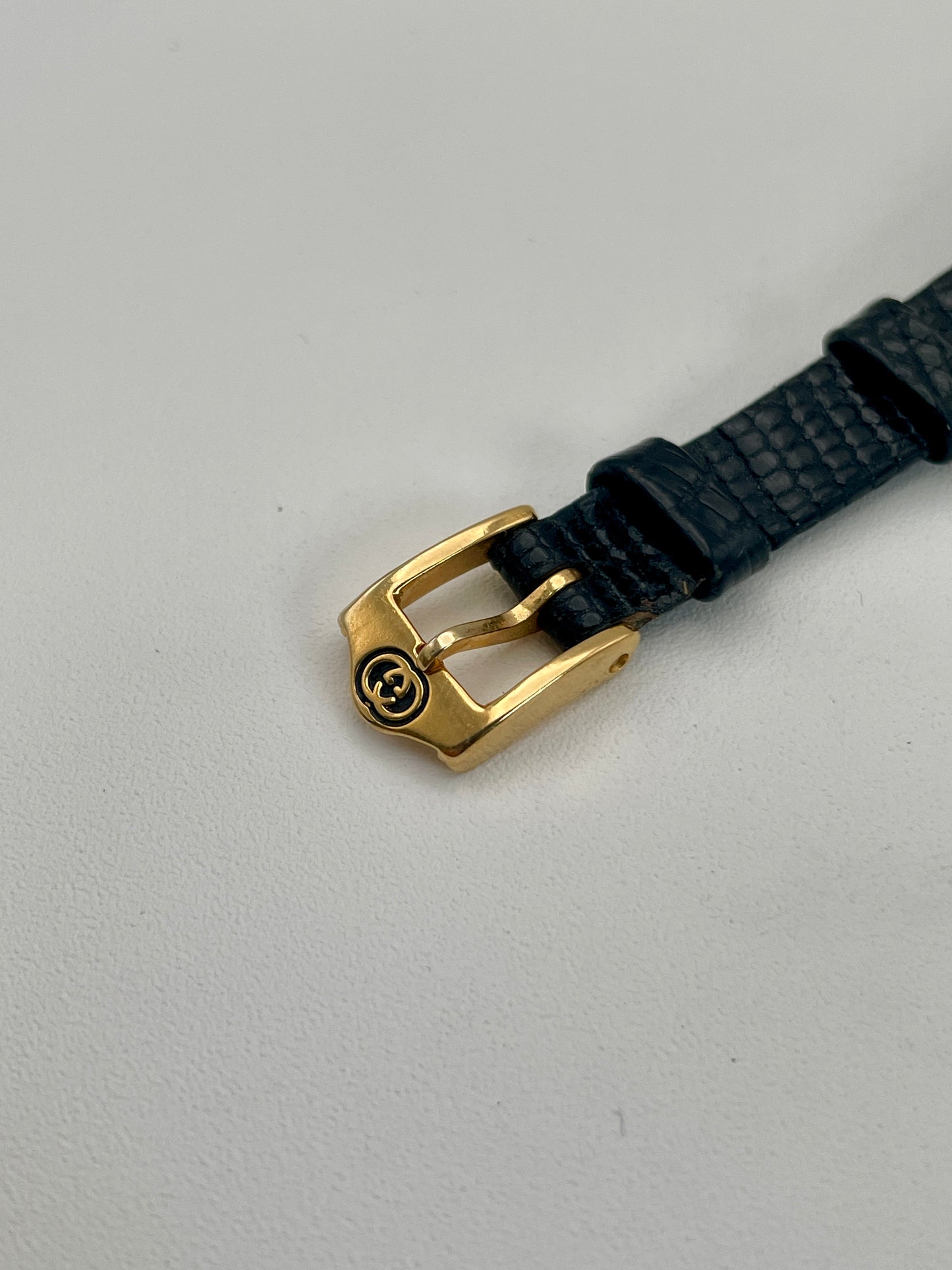 Detailed view of the Gucci Sherry Line watch’s gold buckle, engraved with the Gucci logo.