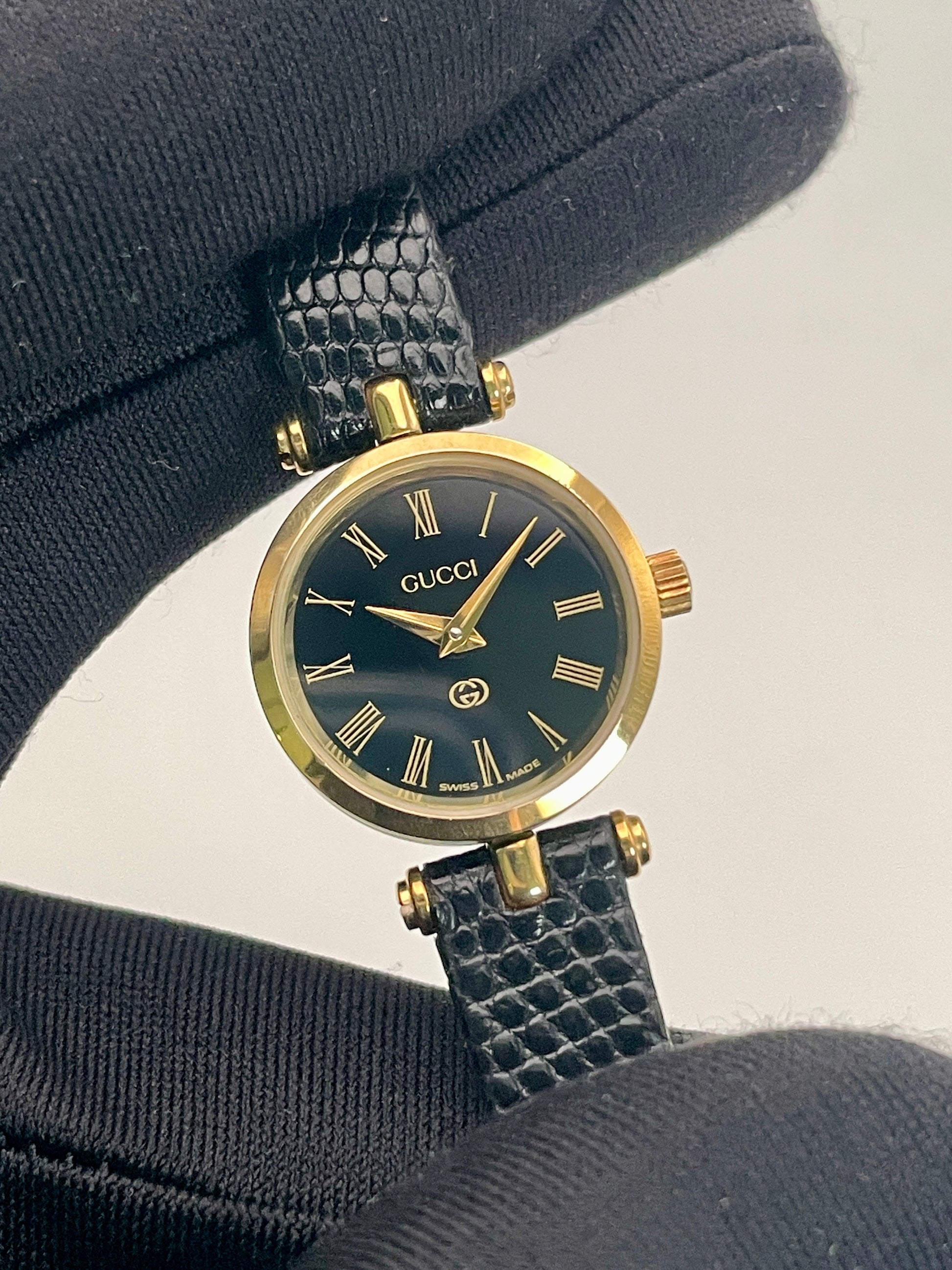 Handheld close-up of the Gucci Sherry Line Vintage Women's Watch in gold, highlighting its elegant black dial and Roman numerals.