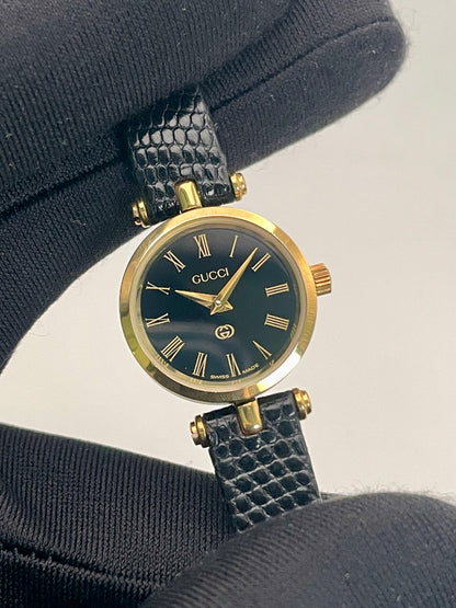 Handheld close-up of the Gucci Sherry Line Vintage Women's Watch in gold, highlighting its elegant black dial and Roman numerals.