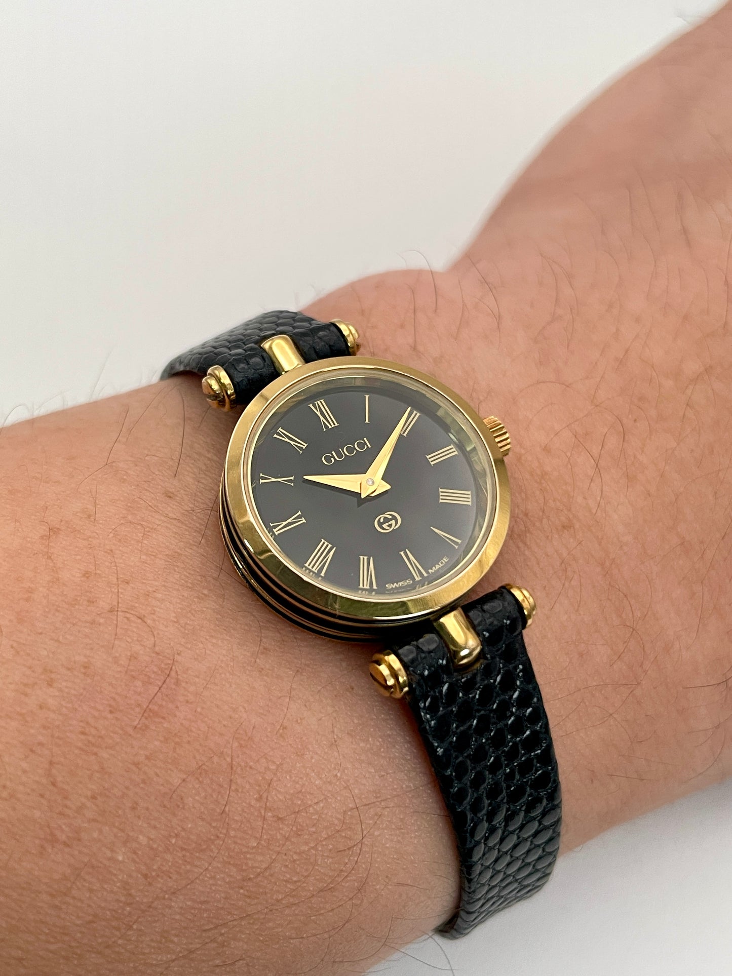 Wrist view of the Gucci Sherry Line Vintage Women's Watch in gold, styled with a textured black leather strap.