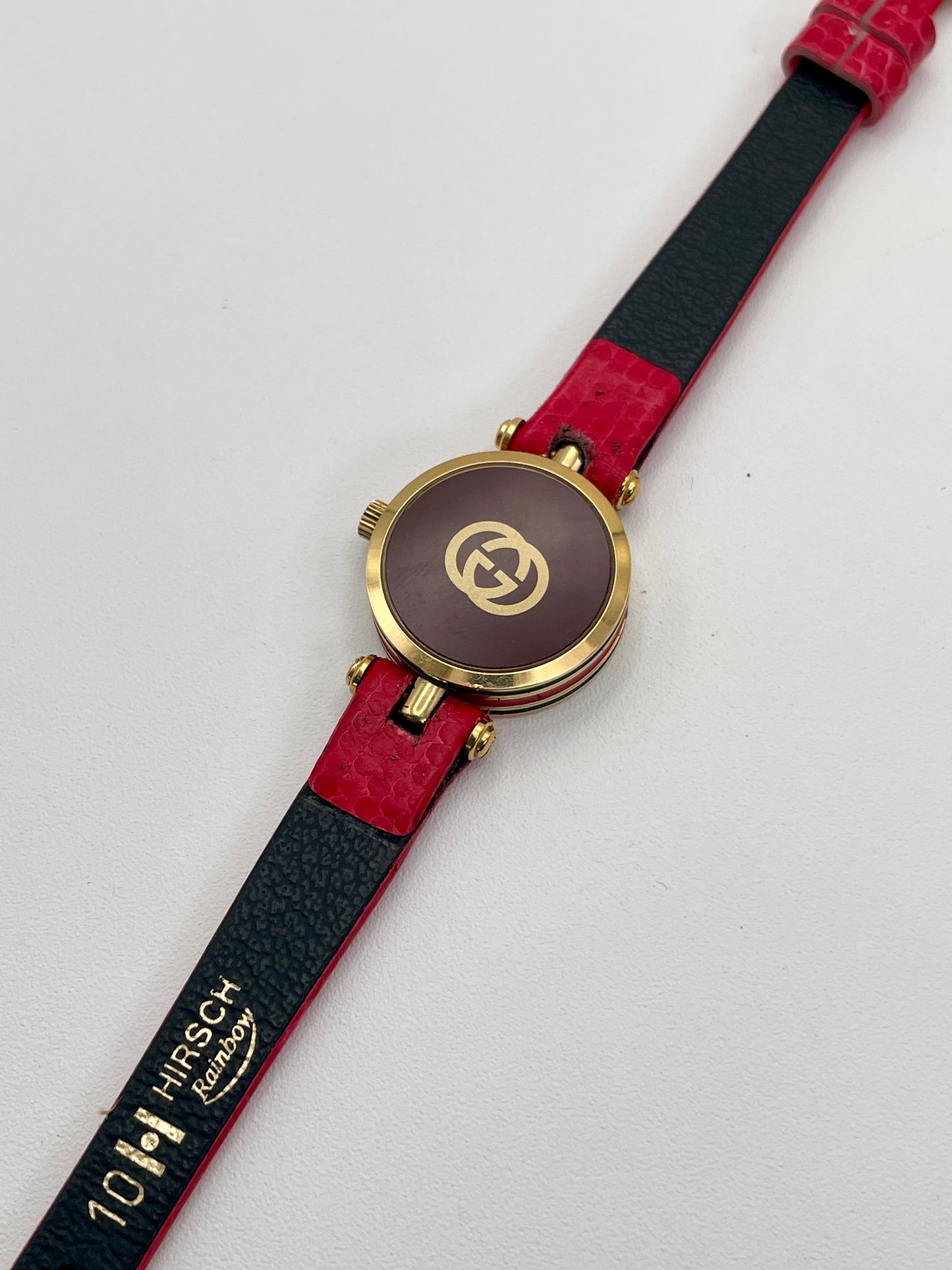 Caseback view of the Gucci watch featuring the brown back cover with gold GG logo and red strap.