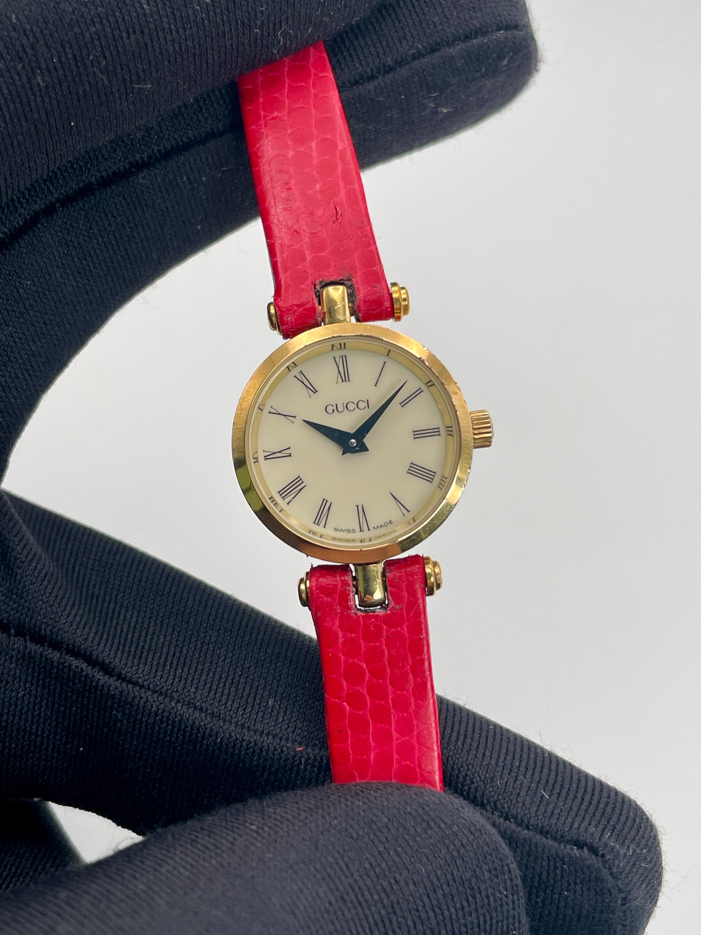 Close-up view of the Gucci watch dial with Roman numerals and gold case, held by a gloved hand.