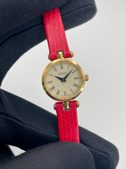 Close-up view of the Gucci watch dial with Roman numerals and gold case, held by a gloved hand.