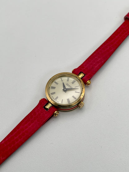Diagonal front view of the Gucci Sherry Line watch highlighting the gold case and red strap.