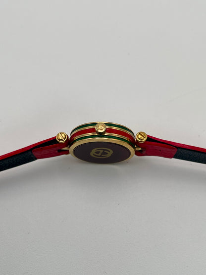 Side view showing the Gucci-branded crown and the signature green-red-green enamel strip around the case.