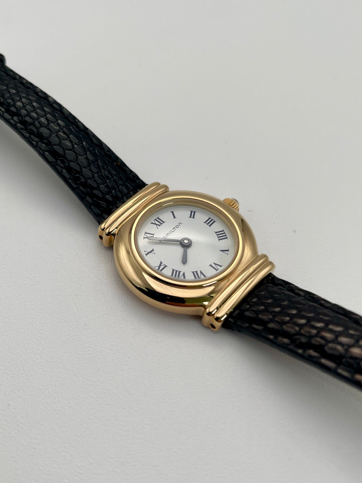 Hamilton 8208 vintage gold watch with a round case, white Roman numeral dial, and black leather strap.