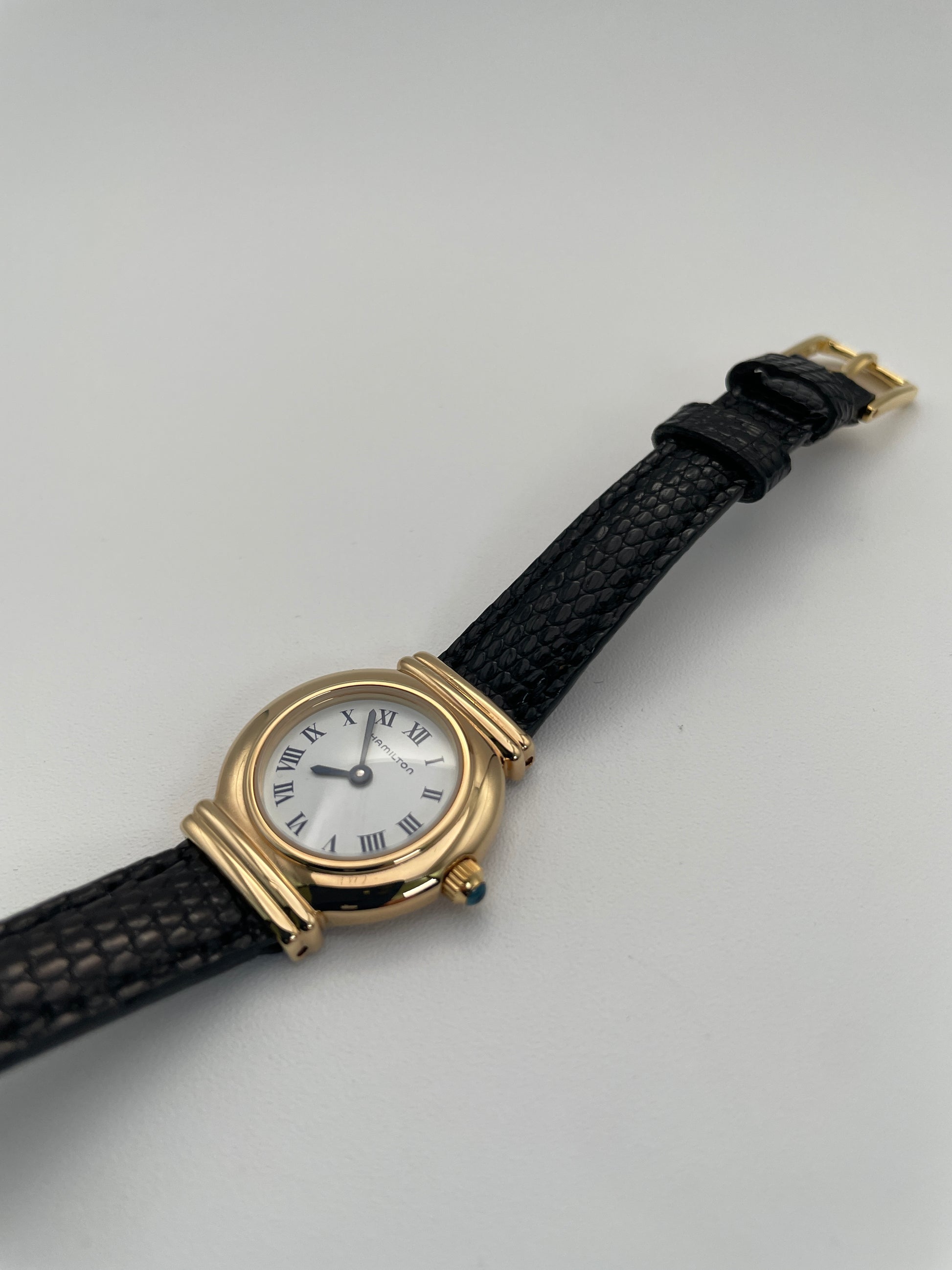 Side crown view of Hamilton 8208 vintage gold watch showing the gold crown and round case with black leather strap.