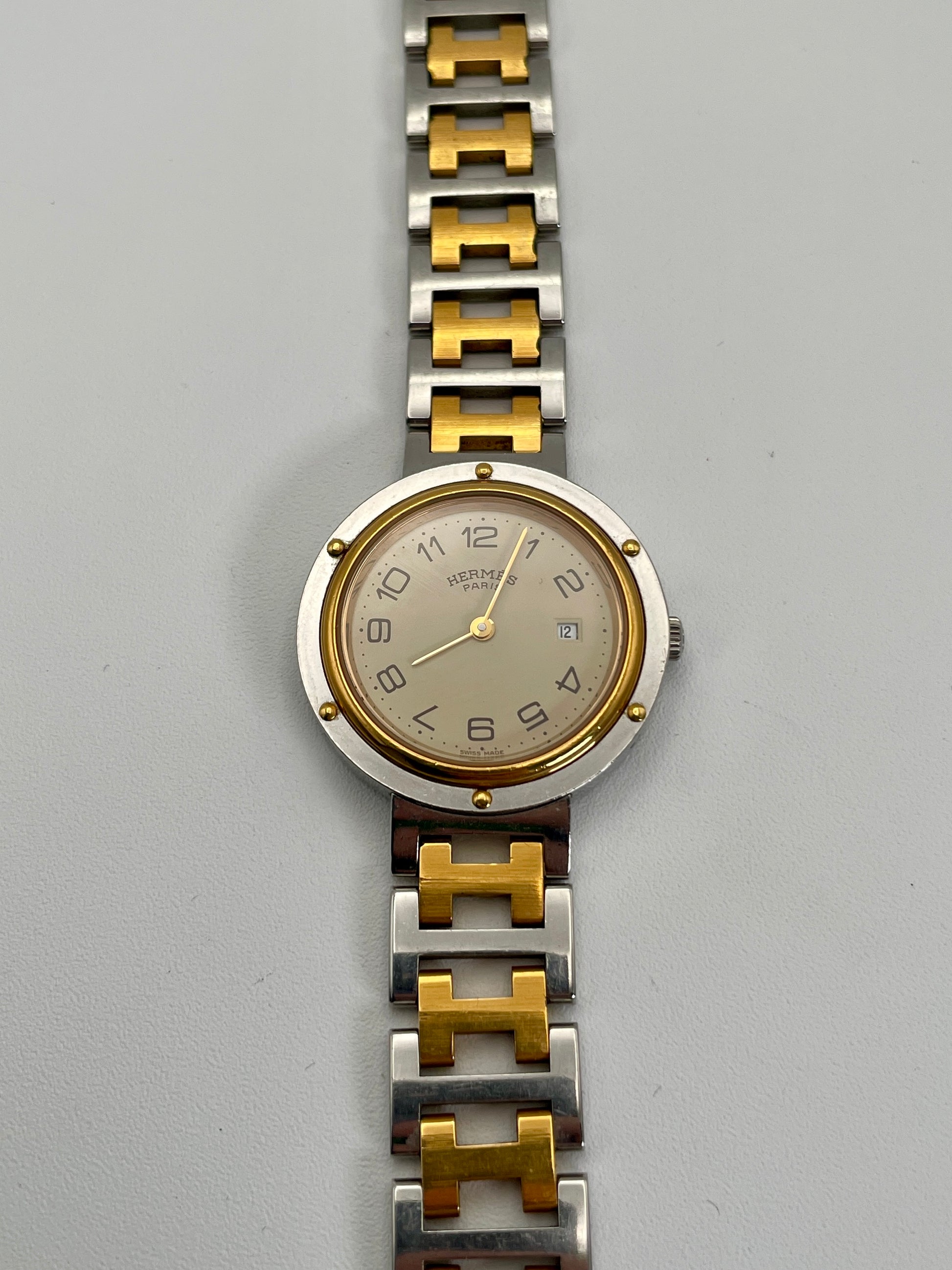 Front view of a Hermes Clipper 30mm two-tone watch in its original box, accompanied by a certificate of origin and guarantee. The two-tone stainless steel and gold bracelet and silver dial are prominently displayed.