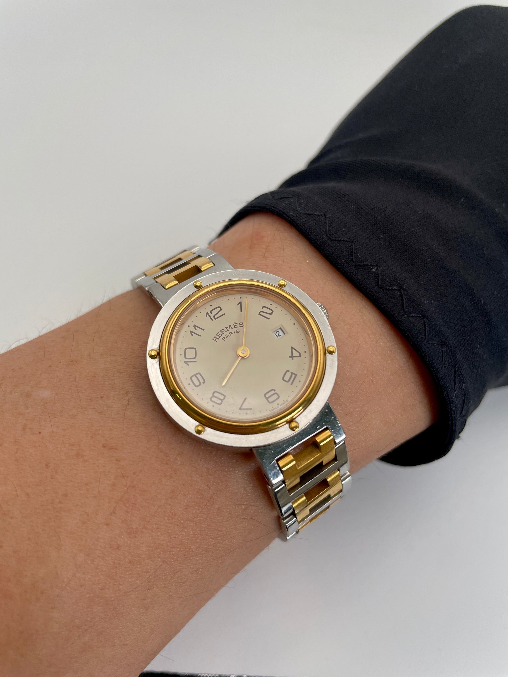 rist shot of the Hermes Clipper 30mm two-tone watch with a stainless steel and gold bracelet, and a silver dial with Arabic numerals and a date window.