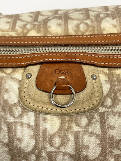 Close-up of the detail on the Christian Dior Trotter Romantique Bag in beige leather and canvas, with a brown leather pull tab.