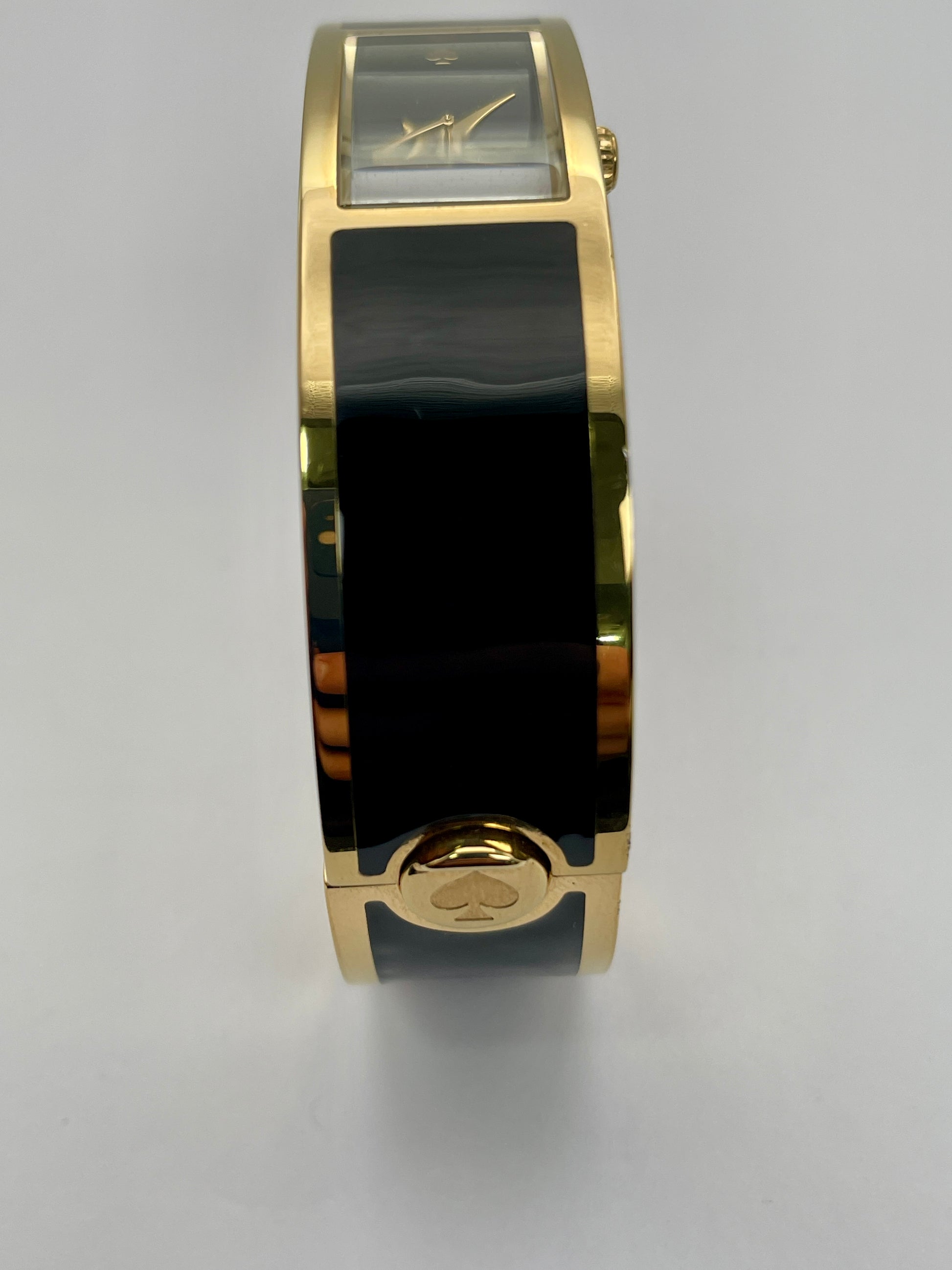 Clasp of Kate Spade Bangle watch highlighting the round gold-tone case and gold tone release clasp engraved with an ace.