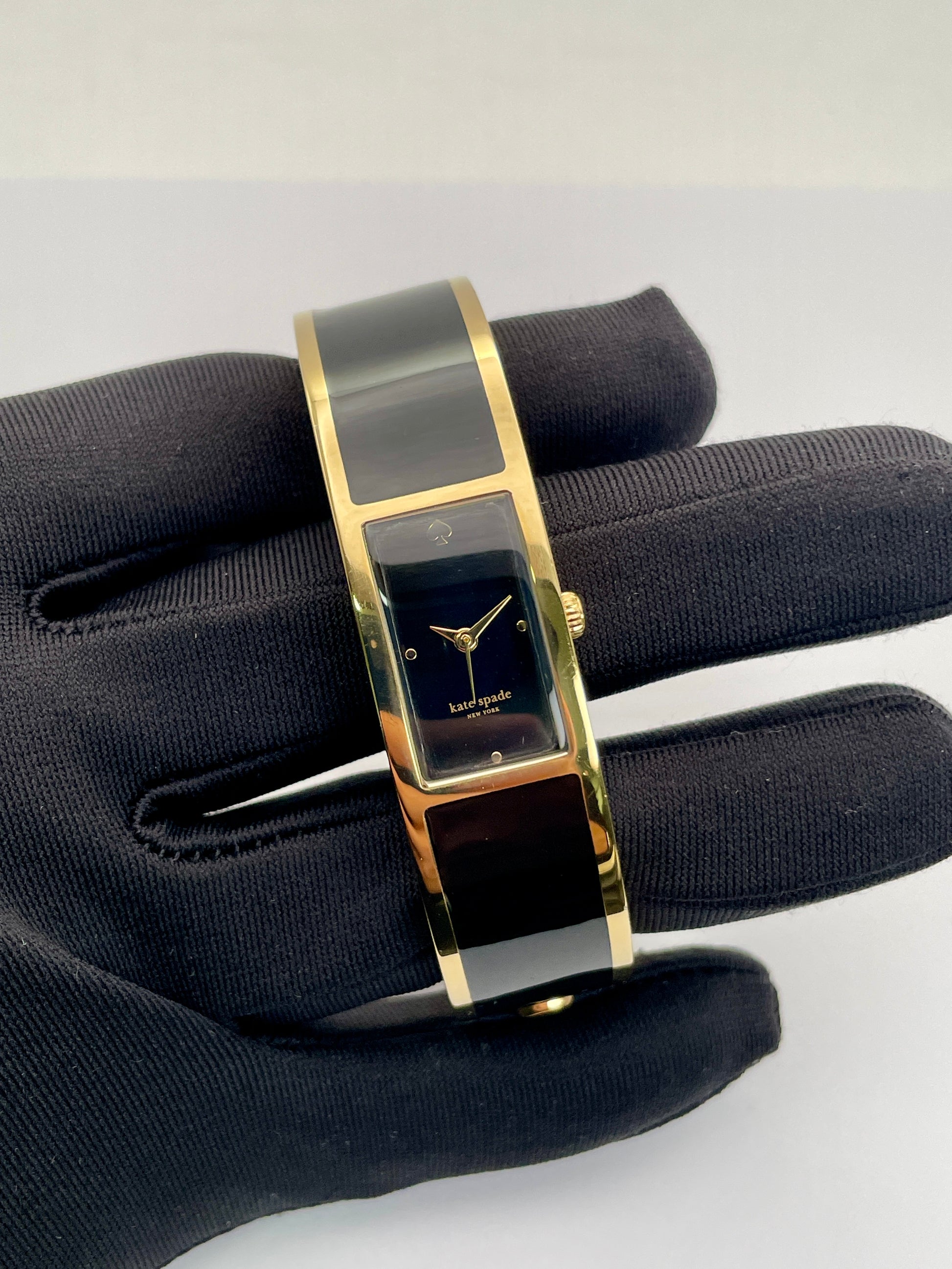 Close-up view of Kate Spade Bangle watch showing detailed craftsmanship of the gold-tone case, gold sword hands and black rectangular dial.