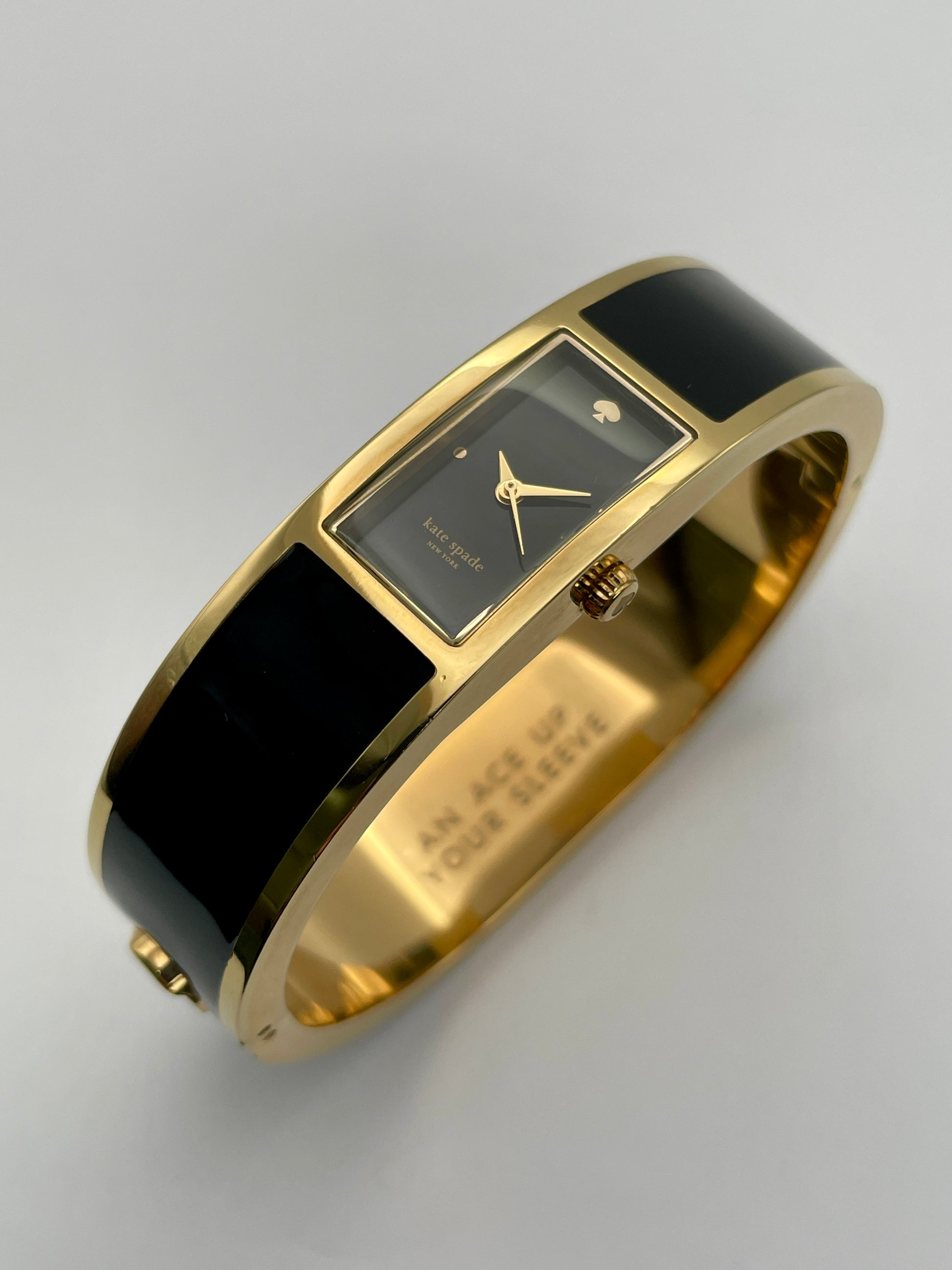 Diagonal View of Kate Spade Bangle watch with a gold-tone round case, black rectangular dial, and black enamel body