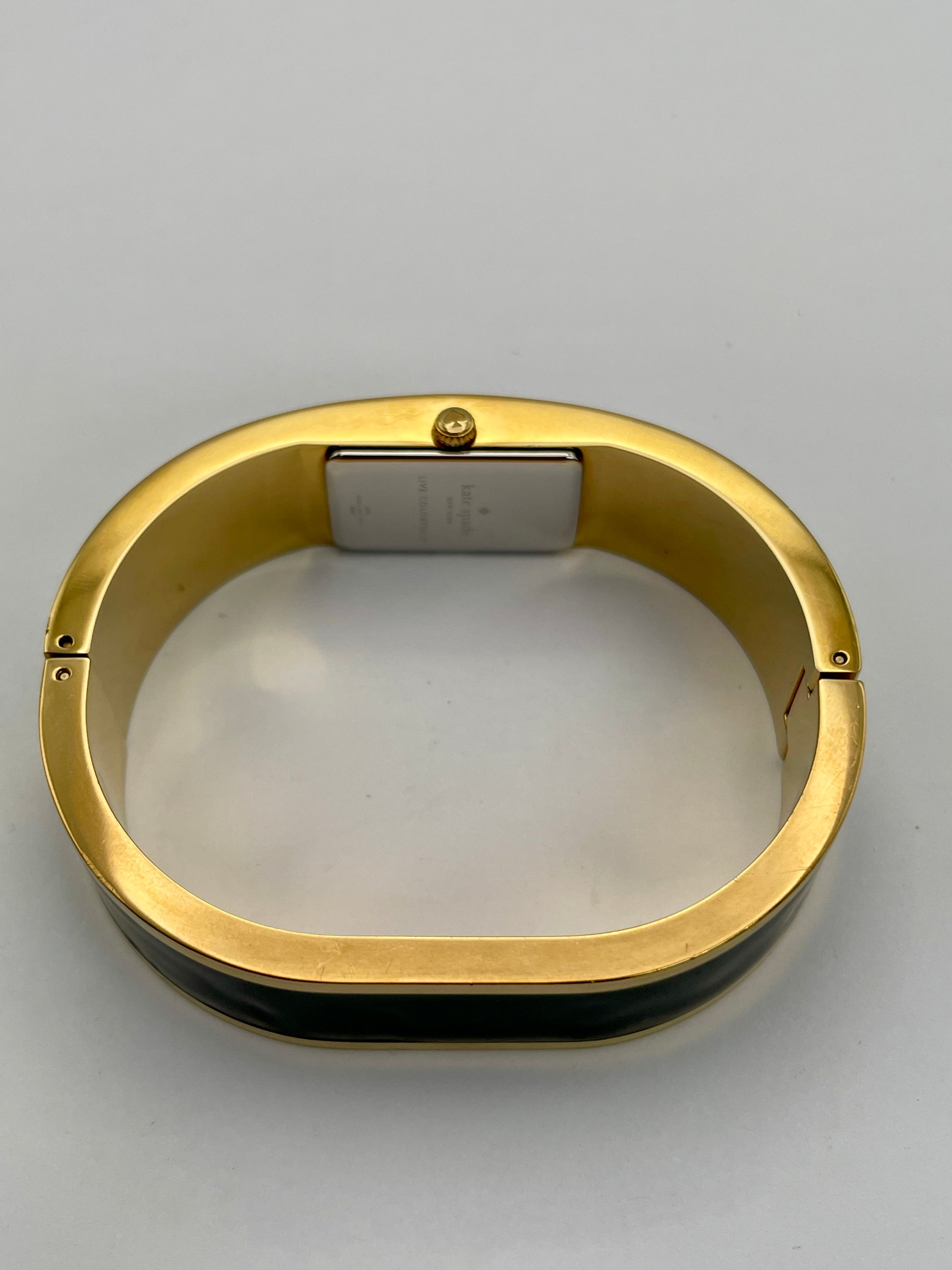 Side crown view of Kate Spade Bangle watch highlighting the round gold-tone case and black enamel body.