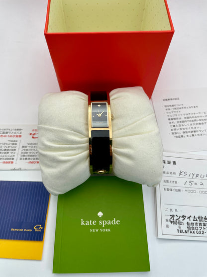 Kate Spade Bangle watch with a gold-tone round case, black rectangular dial, and black enamel body shown with complete inclusions, papers, and box.