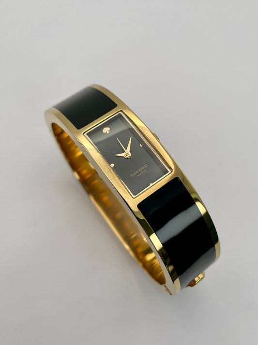 Kate Spade Bangle watch with a gold-tone round case, black rectangular dial, and black enamel body