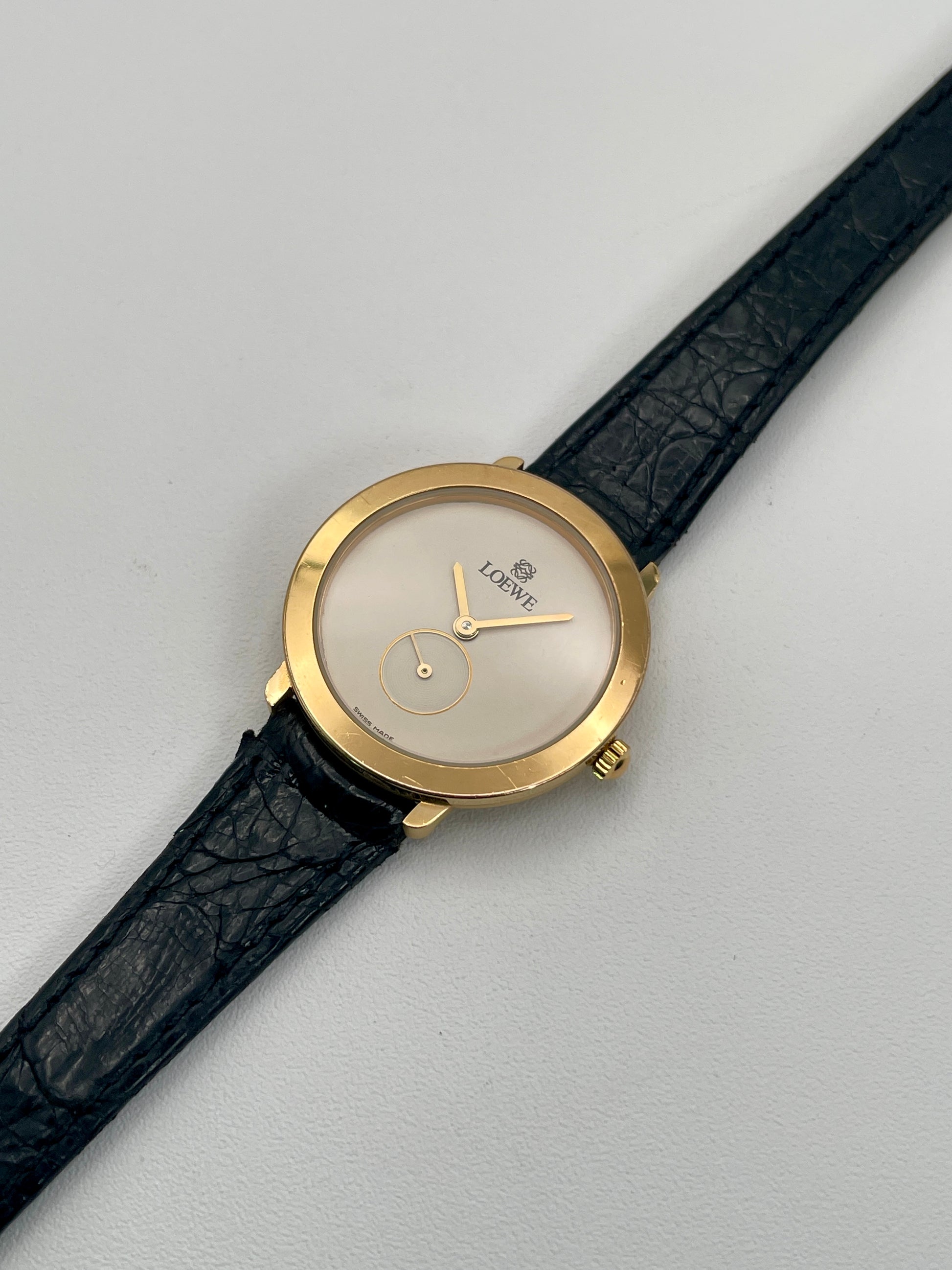 Diagonal view of the Loewe Calatrava gold watch showing the minimal white dial and gold accents.