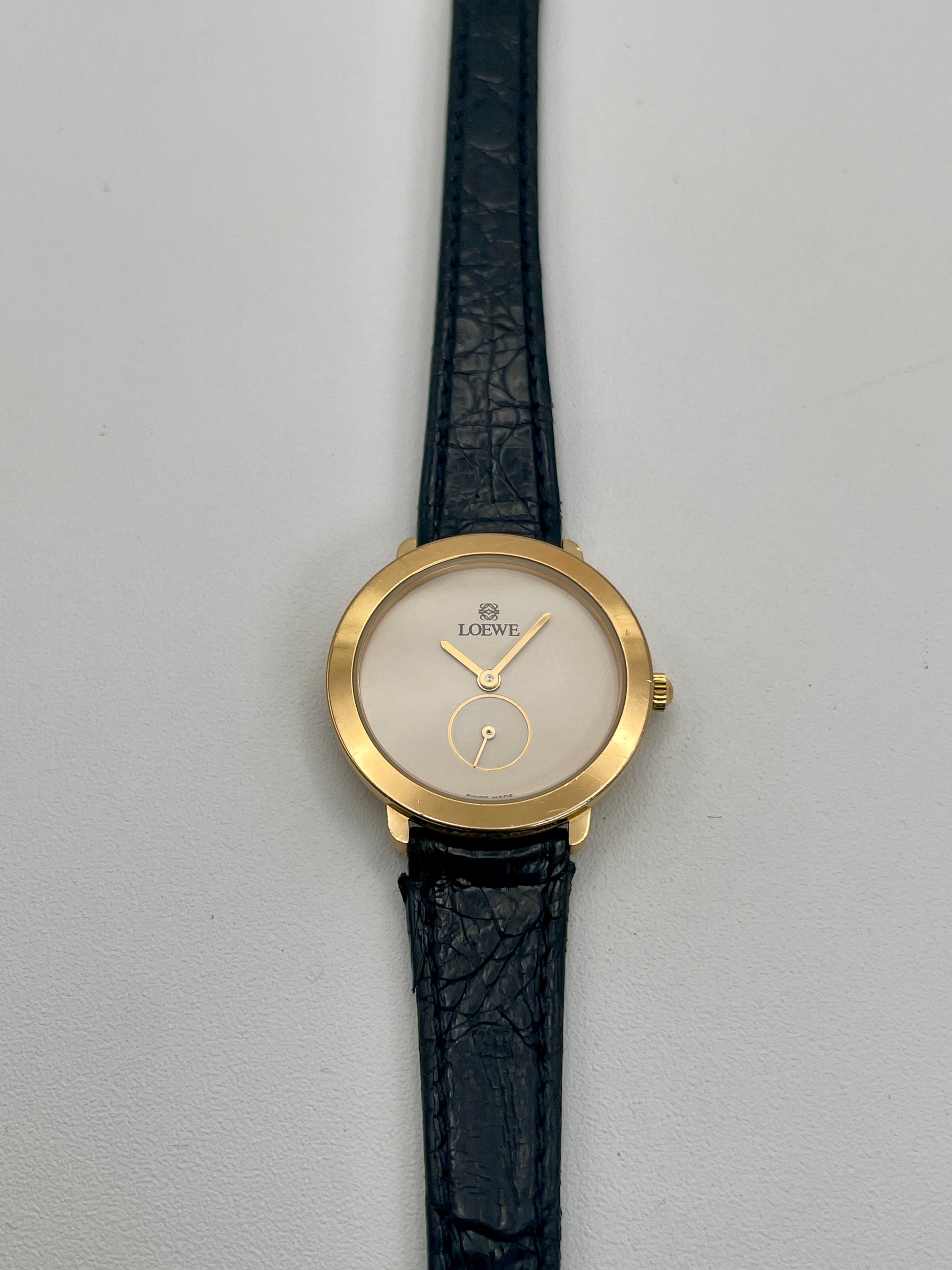 Front view of Loewe Calatrava Vintage Women's Watch in gold case with black leather strap showing white dial and small seconds subdial.