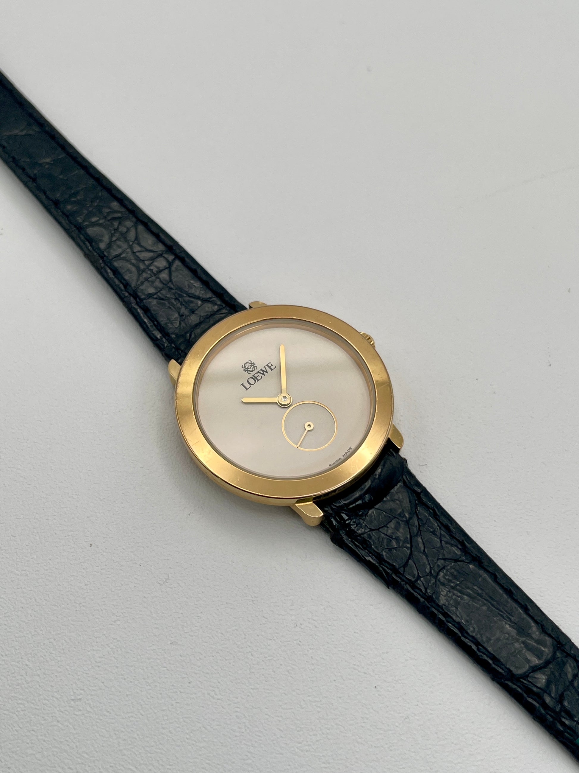 Loewe Calatrava Vintage Women's Watch in gold case with black leather strap showing white dial and small seconds subdial.