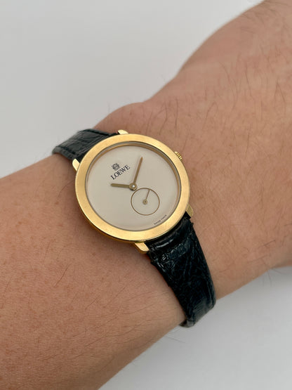 Wrist shot showing the Loewe Calatrava gold watch worn on the wrist with black leather strap.