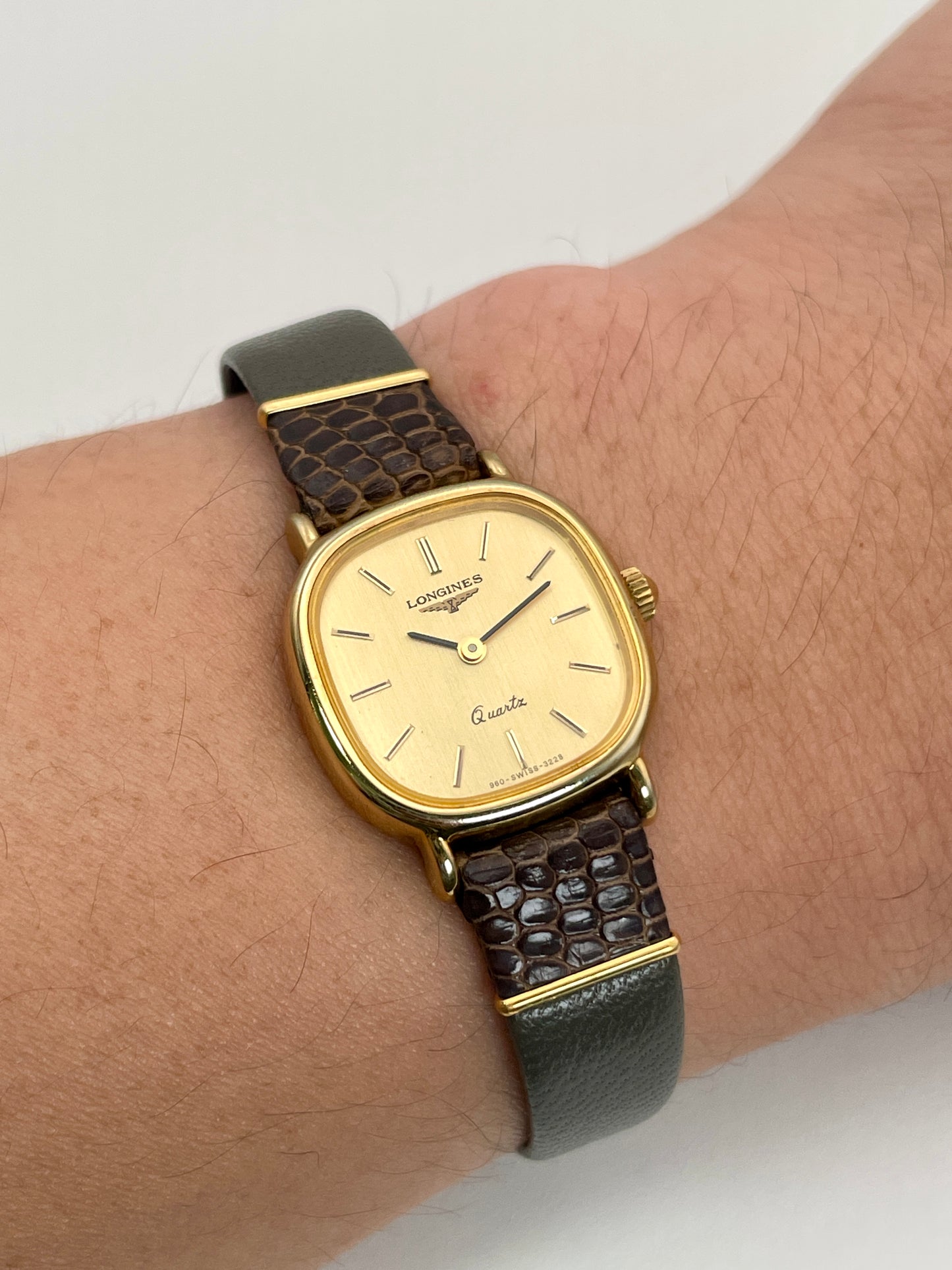 Longines 960 vintage women's watch worn on a wrist, showcasing its gold-tone case and grey leather strap.