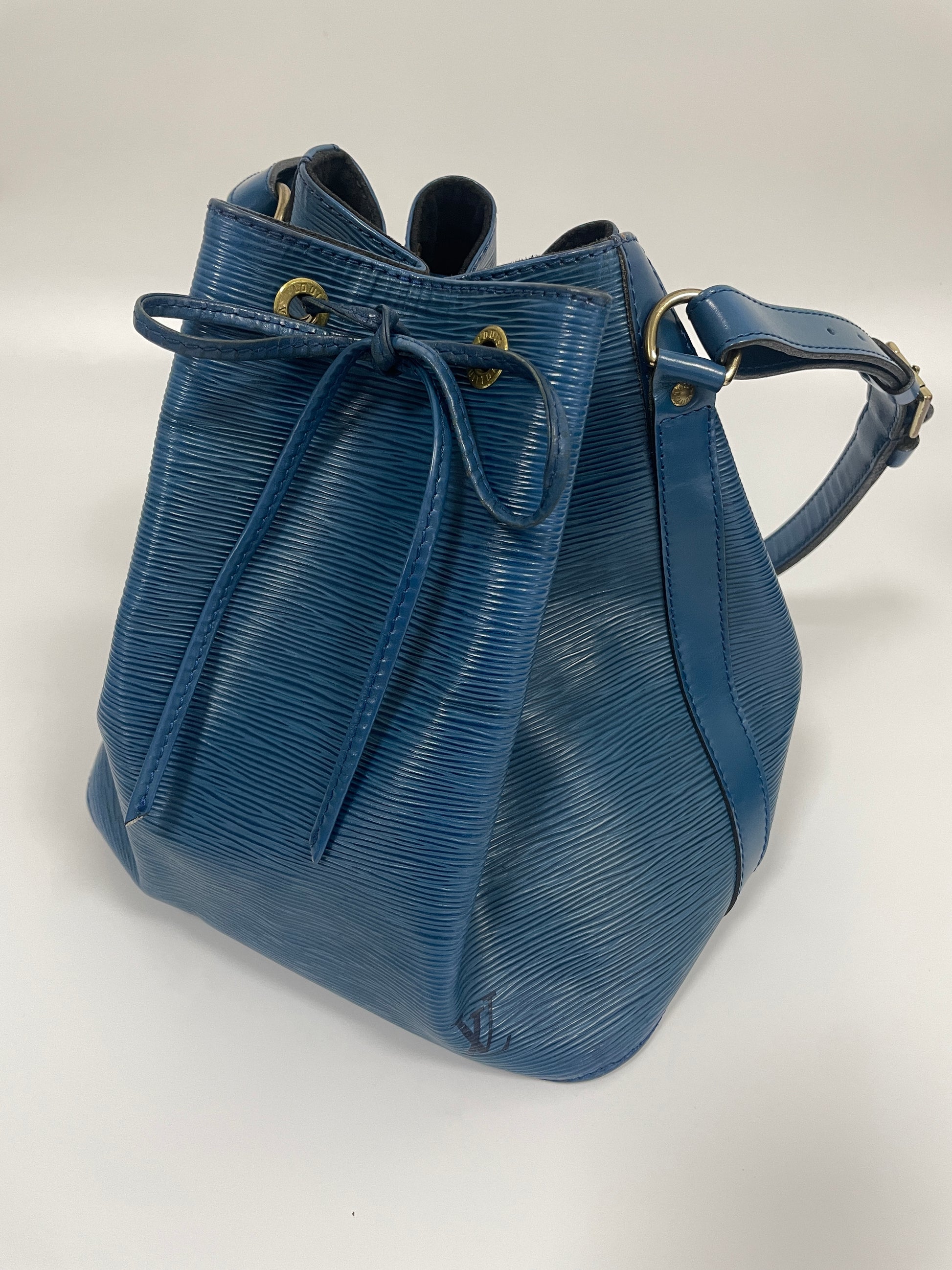 Side profile of the Louis Vuitton Petit Noé Shoulder Bag in Toledo Blue leather, highlighting the bag's structured silhouette and strap.