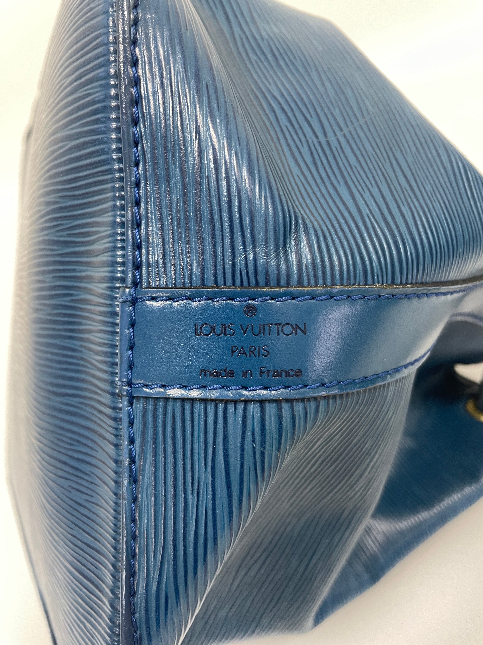 Close-up of the Louis Vuitton logo stamp on the base of the Petit Noé Shoulder Bag in Toledo Blue Leather, made in France.