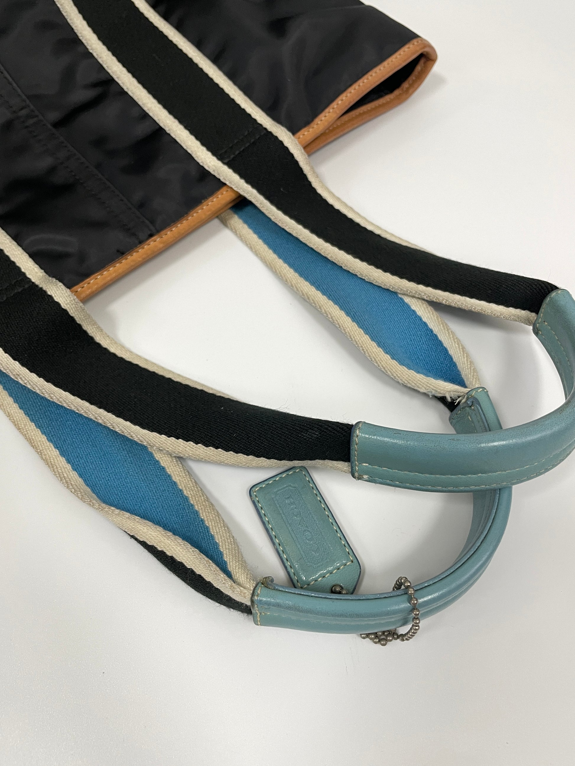 Close-up of the striped handles of the Coach Hampton Tote Bag, with light blue leather accents and a Coach tag.