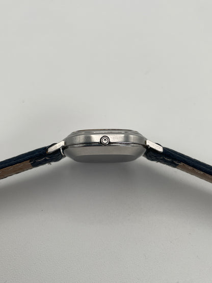 Side view showing the crown of Omega 591.0016 vintage quartz watch with an oval-shaped silver case and blue leather strap.