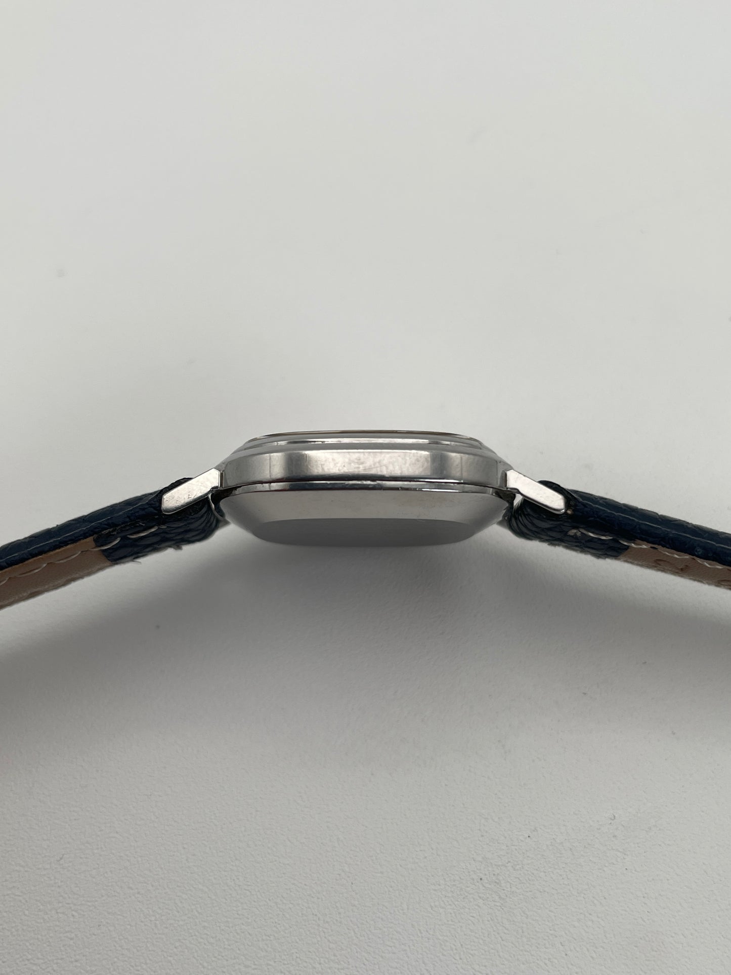 Side view of Omega 591.0016 vintage quartz watch with an oval-shaped silver case, slim profile, and blue leather strap.