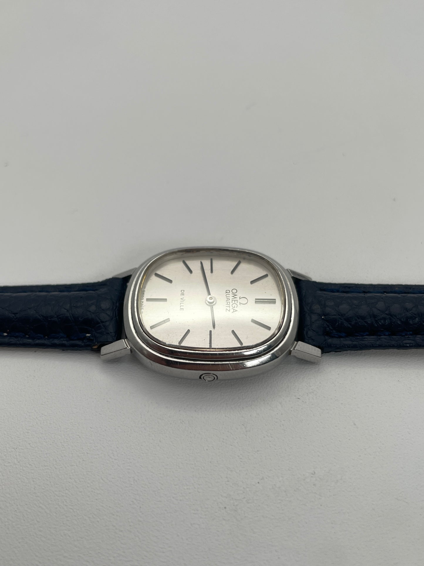 Side view showing the crown of Omega 591.0016 vintage quartz watch with an oval-shaped silver case and blue leather strap.