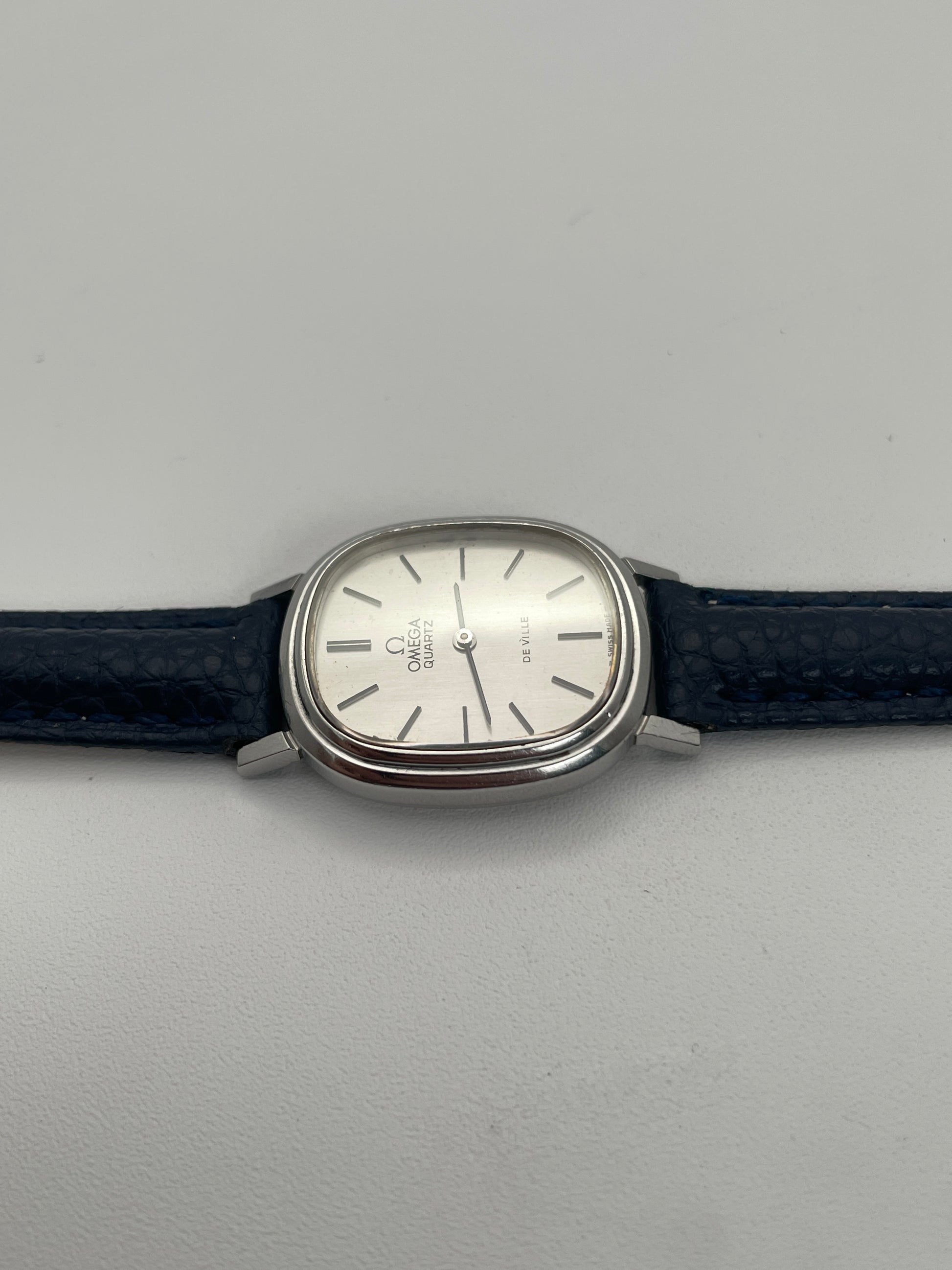 Side view of Omega 591.0016 vintage quartz watch with an oval-shaped silver case, slim profile, and blue leather strap.