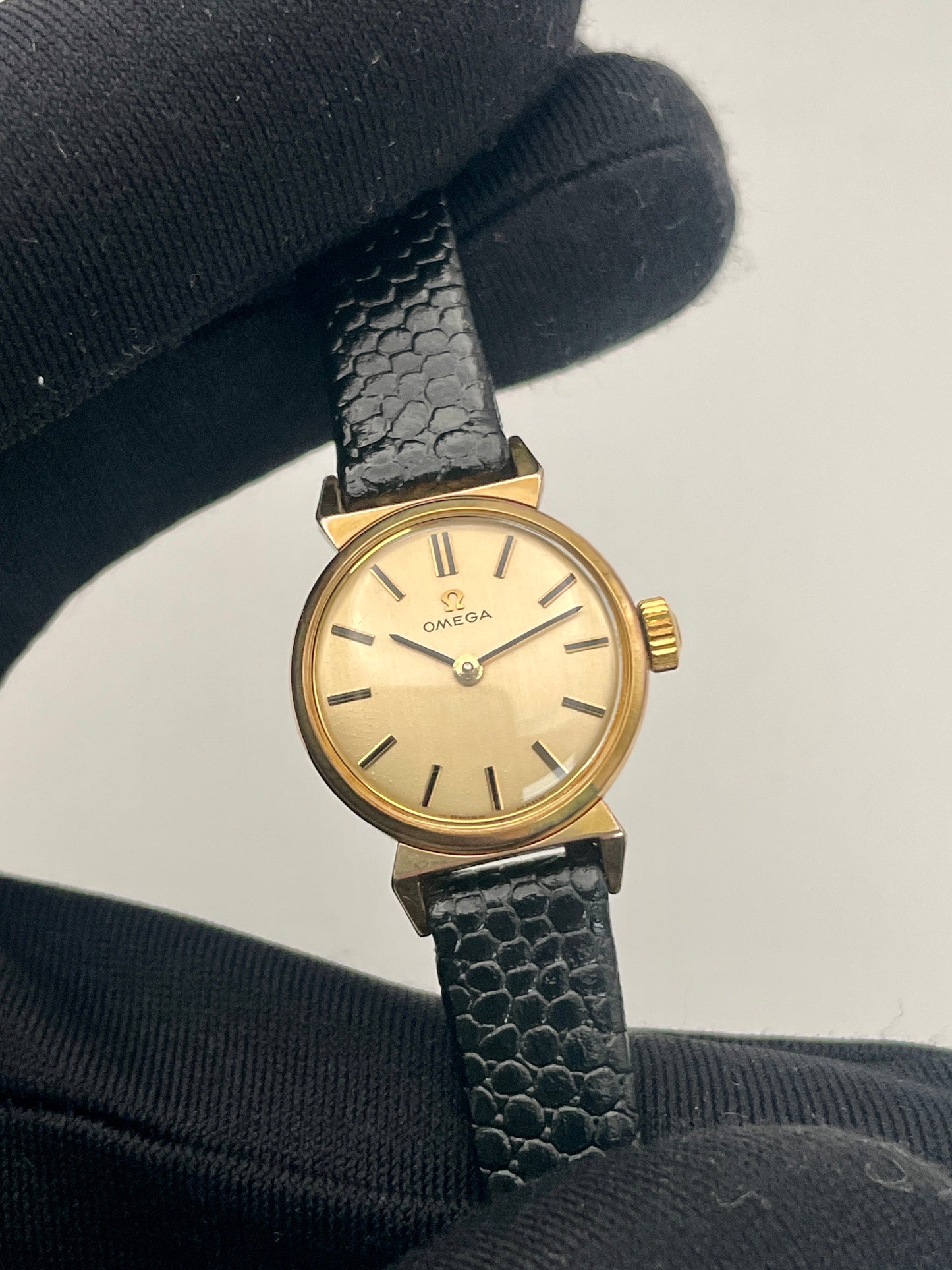 Omega Art Deco vintage gold ladies watch held with a black glove, showing dial and case.